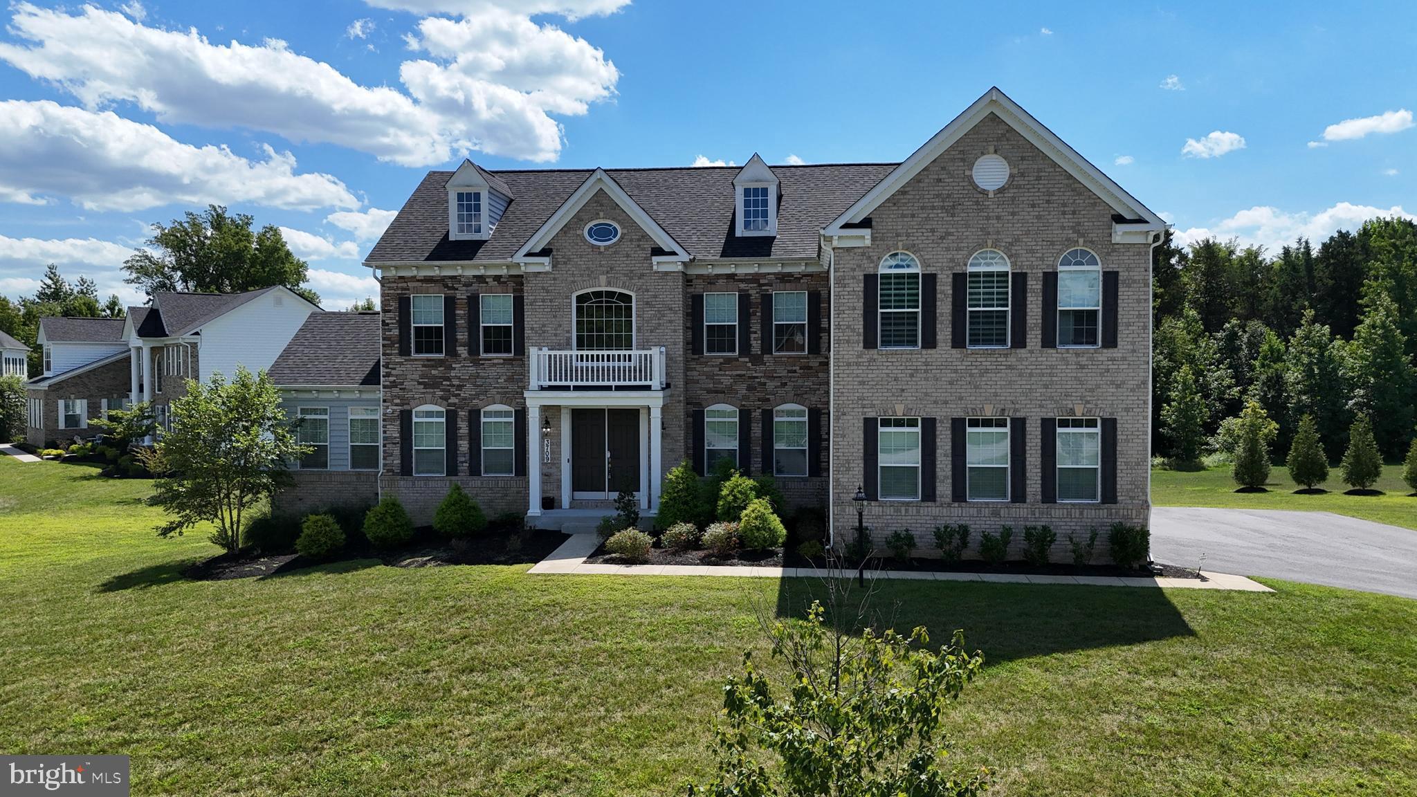 Welcome to this stately Caruso Kingsport model built in 2020, perfectly nestled on a premium lot in Collingbrook Estates. The exterior showcases a regal brick front with a colonial portico, a lushly manicured lawn, and the privacy of mature trees lining the rear. An expansive driveway and oversized three-car garage set the tone for both elegance and practicality. Step inside to a grand two-story foyer with a waterfall staircase accented by white oak treads, crisp white risers, crown molding, and recessed lighting, all set against a soothing neutral palette. To the right, the formal dining room impresses with double tray ceilings and custom window treatments, while the formal living room to the left mirrors this refined aesthetic. The home unfolds into a breathtaking cathedral-ceiling conservatory with Palladian windows, a ceiling fan, and a private TRX balcony with a pergola—an inspiring retreat of natural light and views. At the heart of the home lies the two-story great room, designed to dazzle with soaring coffered ceilings, south-facing Palladian windows with automatic blinds, and a dramatic stone fireplace with custom hearth and mantle. The adjacent gourmet kitchen is a chef’s dream, offering granite countertops, 42” custom slate cabinetry, stainless steel appliances, double ovens, a gas cooktop, built-in microwave, dual sinks including a prep sink on the oversized island, pendant lighting, a butler’s pantry, and a command center with glass cabinetry. The main level also features a thoughtfully designed in-law suite with French door entry, crown and chair rail moldings, and an attached full bath with walk-in shower, perfect for guests or multi-generational living. A mudroom, powder room, and access to the expansive garage complete the main level. Upstairs, the presidential suite awaits with double door entry, tray ceilings, crown molding, and luxury vinyl flooring. A sitting area with cathedral ceilings, automatic shades, and an electric fireplace creates the ultimate retreat. The California spa bath boasts dual vanities with stone counters, a Roman shower with bench, a private water closet, and a walk-in linen closet, accompanied by two custom walk-in closets. Three additional bedrooms with plush carpeting, two upgraded full baths, and a laundry room complete the upper level. The fully finished lower level is a showstopper, featuring two bonus rooms, a full bath, a media room with tiered seating, a recreation space, rough-in for a kitchenette, and an additional laundry hook-up. A walk-out entry leads to the double-tiered paver patio, perfect for entertaining or relaxation. The backyard is an oasis with a massive TRX deck, screened-in gazebo with professional lighting, a retaining wall, and lush greenery, offering the perfect balance of luxury and privacy. Located in the highly sought-after Collingbrook Estates, this home offers the best of both worlds—peaceful surroundings with convenient access to major commuter routes including Route 50, I-495, and the BW Parkway, as well as proximity to Bowie Town Center, dining, grocery stores, and entertainment options. This residence is a rare combination of luxury, comfort, and thoughtful design—an extraordinary place to call home.