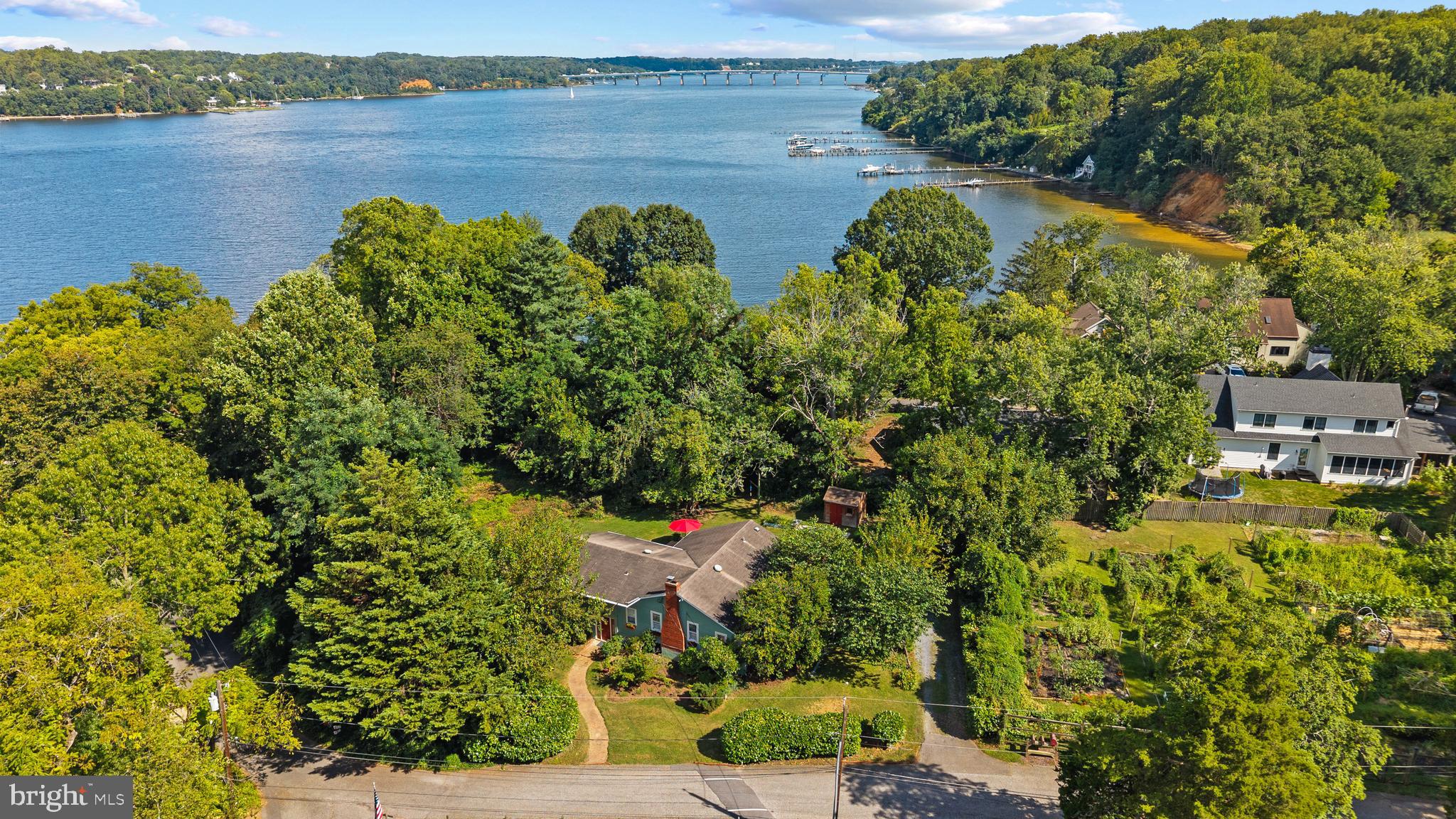 A true piece of Epping Forest history, this storybook coastal-style cottage—originally built in 1926 as the community’s “Tea House” sales office—welcomed buyers arriving by boat with tea by the fireplace. Today, it remains a one-of-a-kind property, offering seasonal views of the Severn River and Drevar Park (October through June), a spacious flat yard, and an unmatched sense of privacy.
The sale includes two adjacent water-view lots directly in front of the home, bringing the total to .50 acres. This rare offering preserves the cottage’s view and ensures a natural, wooded buffer —creating a private oasis within this beloved neighborhood.
Inside, the cottage offers cozy living spaces with three or four bedrooms, two full baths, an office, and a family room currently serving as a spacious primary bedroom and reading nook with a view. Recent updates within the past three years include fresh exterior and interior paint, a new HVAC system, new carpeting, an office window, patio door, and updated appliances (electric range, microwave, refrigerator).
Rich in history and character, the home lends itself to many possibilities—whether a vacation retreat, year-round residence, or a canvas for something larger.
Enjoy the coveted waterside lifestyle of Epping Forest, a gated community with a marina, beach, clubhouse, community garden, and tennis/pickleball courts. Residents delight in summer camp, volleyball league, and year-round festivities, including a 4th of July parade with fireworks, an Easter egg hunt, and the always-anticipated Labor Day cardboard boat race. All just minutes from downtown Annapolis and Route 50. Epping Forest is a Special Tax District, ($1742.91/yr.) with binding Rules and Regulations. Welcome Home!