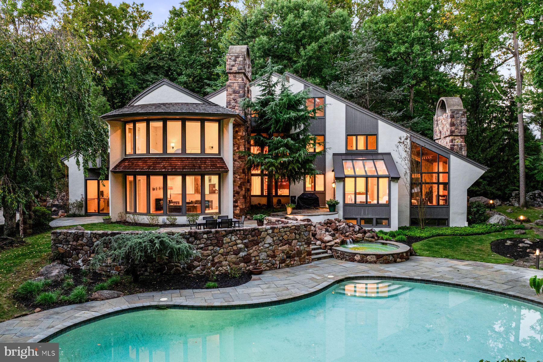 In one of Chester County’s most prestigious neighborhoods, this secluded 8,500 sq ft estate offers nearly four acres of private, luxury living with sweeping forest and stream views, a heated pool and spa, breathtaking architecture, and light-filled interiors crafted for both grand entertaining and everyday comfort.
Approach the property from a hidden extension off an already-quiet cul-de-sac, and be welcomed by a stunning stone driveway, additional stone-lined guest parking, and charming stone steps leading through the yard to the front entry. Approaching the home, you’ll notice the privacy and rare connection to nature, while enjoying the warmth of a neighborhood where homes are hidden from view yet close enough for a friendly community feel. The convenient location is unparalleled, with shopping and dining on the Main Line just minutes away, as well as the nationally acclaimed T/E School District. This unique combination- private retreat in nature with top-tier schools and local amenities minutes away- is rarely found.
Here, mornings begin in a peaceful habitat where you wake to birdsong and rustling leaves, and enjoy your coffee while watching deer, chipmunks, and turtles visit from the surrounding forest. Designed by acclaimed architect Mark Stanish and crafted by Pohlig Builders, the home offers light-filled spaces with beautiful forest views from every room.
The primary bedroom is a true haven with a curved wall of windows, a deck overlooking the wooded grounds, and a 14-foot heated cathedral ceiling. The spa-like bath features a two-person Jacuzzi with marble surround, heated floors, a seated shower, and dual walk-in closets.
The soaring 3-story travertine foyer sets the tone for welcoming guests, framed by dramatic walls of windows. The spacious living room features oak floors, a gas fireplace with carved stone mantel, and glass doors opening to a slate terrace with forest and stream views. The formal dining room dazzles with marble floors and sliders to a private deck, perfect for intimate dinners. Multiple home office spaces invite creativity, with gorgeous views, unique rooflines, and oak floors.
At the heart of the home, the chef’s kitchen is outfitted with Gaggenau gas cooktops, a grilling station, induction cooktop with range hood, Bosch dishwasher, Sub-Zero refrigerator/freezer and ice maker, double ovens, and abundant cabinetry and prep space. The sun-drenched breakfast room, with windows on all sides, opens directly to the terrace and outdoor grilling area, while the adjacent family room boasts an 18-foot vaulted ceiling, built-in cabinetry, a stone fireplace, and floor-to-ceiling windows bringing the outdoors in.
The expansive lower level is an entertainer’s dream, with a wine tasting room and classic brick wine cellar for 550 bottles, an Art Deco kitchenette, custom bar, and refreshed recreation spaces including a finished exercise room, pool table room, media room with fireplace, automated shades, movie-size TV, and game zone with foosball and air hockey—ideal for movie or pizza nights.
Outside, the heated pool and spa form a boutique-resort oasis beneath a canopy of trees, with surrounding flora, outdoor speakers, and subtle lighting for both sunny afternoons and evening swims.
With its rare blend of natural beauty, architectural sophistication, and premier location, this property is more than a home—it’s a private sanctuary where luxury, design, and nature exist in perfect harmony, just minutes from the heart of the Main Line.