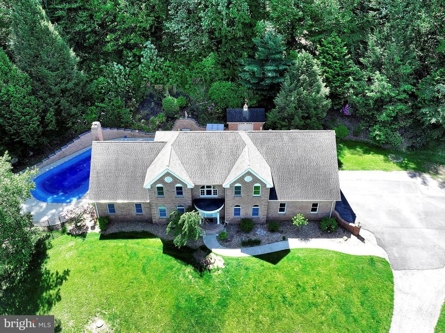 As you turn onto the private drive and pass the tranquil stream, you will immediately be captivated by the breathtaking beauty of this estate situated on over 7 private acres. A spacious driveway welcomes you, offering ample parking for all your vehicles and recreational toys. The home features a 3 car side entry garage with oversized doors, perfect for larger vehicles or extra storage. A concrete walkway leads to the stately brick front entrance, setting the tone for the elegance and craftsmanship found throughout the property. Step into a grand 17-foot foyer featuring a stunning curved staircase that sets the tone for this elegant home. To the right, you’ll find a formal living room perfect for entertaining, while to the left, the formal dining room showcases beautiful hardwood floors and flows seamlessly into the gourmet kitchen. The kitchen is a chef’s dream, boasting a massive island with a built-in cooktop and exhaust system, a wall oven/microwave combo, and exquisite cherry cabinetry accented by custom built-ins throughout. Overlooking the kitchen is a spacious family room, offering a bright, open-concept layout. Enjoy the warmth of a dramatic floor to ceiling brick fireplace, vaulted ceilings, and skylights that bathe the space in natural light. The spacious family room overlooks the kitchen, creating a seamless and bright open-concept living area. Anchoring the space is a stunning floor to ceiling brick fireplace, complemented by soaring vaulted ceilings and skylights that fill the room with abundant natural light. A generously sized office provides the perfect setting for a home workspace or homeschool area, offering both functionality and privacy. Up the elegant curved staircase, you’ll find four spacious bedrooms and a large open loft area perfect as a TV room, play space, or easily convertible into a fifth bedroom. The primary suite is truly expansive, offering ample space for all your furnishings and more. Enjoy your own private balcony overlooking the backyard, skylights that brighten the room, and three oversized walk-through closets. The luxurious en-suite bathroom features a tiled shower built for two, a relaxing jacuzzi tub, dual vanities, and built-in heat lamps for added comfort.
Three additional generously sized bedrooms and a full hall bath with another jacuzzi tub complete the upper level. For added convenience, the main-floor laundry includes a second-floor laundry chute.
You won’t believe this incredible finished lower level designed for ultimate fun and entertaining. A boat-turned-bar, beachy décor, and a laid-back Margaritaville vibe make it the perfect party space. Separate TV area included, and everything stays! Plus, a ramp from the garage offers easy access for storage.
The exterior is just as impressive an entertainer’s dream! The oversized heated concrete pool features a separate hot tub for year-round enjoyment. A convenient pool house is perfect for hosting summer gatherings, and ample storage space keeps everything organized all year long. 3 car garage and ample parking in the driveway.