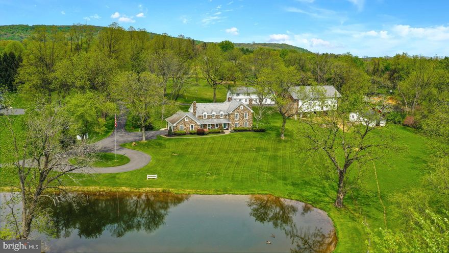 Sweeping lawns, a park-like setting, more than 7 magical acres, an 1800’s stone bank barn, an historic stone limekiln and a willow shaded pond are just part of the magic of this Saucon Valley classic. A long drive crosses a lovely stone bridge over the Black River Creek and leads to a reproduction, stone Pennsylvania farmhouse. Long admired by neighbors and passersby, your own treasured memories are just waiting to be made here. The home was designed and built with an eye to a rich history, where many original historic elements create this perfect setting. There is a gracious front porch overlooking pond and pastures, a covered back porch and paver patio and a second floor covered deck for morning coffee. Inside, beamed ceilings, moldings, built-in bookshelves and wide plank flooring complement the rooms. Five fireplaces are found in the formal living room, family room, dining room, LL and master bedroom.  There’s room for everyone, with four bedrooms, a family sized cherry kitchen and lower level recreation and game rooms. The original, stone bank barn has two stalls for horses and provides upper level storage, or what might be a magnificent space for future parties. The adjacent carriage house has been converted to office and guest quarters. This wonderful property has it all - a storybook setting, a flawless blend of old and new eras, and effortless access to all that Saucon Valley has to offer. Bring your dreams and your ideas and build on to the legacy.