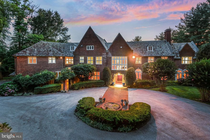 Set on 1.6 acres in sought-after Northside Villanova within Lower Merion Township, this 1924 red brick manor showcases timeless architecture with a slate roof, expansive leaded glass windows, and nearly 9,000 square feet of living space. Set back from the road, the approach is marked by a circular drive and a canopy of mature trees that frame the property with privacy.

The entry vestibule opens to a dramatic foyer with wainscoting, leaded glass windows, and views through French doors to the rear terrace, flanked by the formal living and dining rooms. Natural light, hardwood floors, and detailed millwork set a welcoming tone, while a sweeping staircase with iron railings and a wood handrail rises to a landing with a built-in window seat —a  striking first impression. The generously sized formal living and dining rooms reflect the home’s distinction with high ceilings, paneled walls, and carved limestone fireplaces; six fireplaces in total. French doors continue in nearly every room, extending to large terraces on the rear of the home. The living room opens into a bright sunroom with black and white checkered tile floors, an additional fireplace, while the dining room connects to an all-season room overlooking the rear grounds. Built-in bookshelves and glass-front cabinetry enhance the architectural character of the dining room, while a butler’s pantry, a cozy sitting room with fireplace, and a formal powder room complete this wing.

The kitchen features soaring ceilings, a center island, granite countertops, and generous cabinetry, some with glass-front doors, as well as professional grade appliances. A built-in banquette is framed by two-story windows that provide abundant natural light. An open rear staircase leads to a large second-floor family room that overlooks the kitchen, with built-ins and high ceilings creating a natural gathering place. Next to the kitchen, a mudroom with entry to the garage and driveway adds convenience with an informal powder room, pantry, and coat closet.

At the top of the main staircase, the primary suite commands its own private wing. This large room features paneled walls, hardwood floors, a marble fireplace, and windows framing both front and rear views. A light-filled dressing room connects to the ensuite bath. In the style of homes built in this era, a second primary bath with suana is found on the opposite side of the suite. This bath also opens Jack-and-Jill style to an office (which could be bedroom 6). The configuration continues as this room connects to an additional jack and jill bathroom and an additional bedroom. Off the center hall, two additional updated bedrooms offer ensuite baths. A spacious laundry room is conveniently located nearby. Through the 2nd floor family room, is an additional sitting room and adjoining bedroom also has an ensuite bath. It could serve as an in-law or au pair suite, or a homework room. In total the home offers 5/6 Bedrooms and 6 full baths.
The lower level offers a large area with daylight windows, providing potential for future finishing. This level also includes a wine cellar and additional storage spaces.

The rear grounds are designed for both recreation and relaxation, featuring an expansive terrace, an inground gunite pool and pool house w/ 2 bathrooms/changing rooms, washer/dryer, kitchenette.  Also side tennis/basketball sport court. Mature trees and gardens frame the setting and provide privacy. A side entry attached garage has 2 bays.

Located in the award-winning Lower Merion School District and close to many of the area’s private schools as well as renowned country clubs, the Villanova train station just one mile away, and I-476 for easy access to Philadelphia.

717 N. Spring Mill Road is a distinguished Main Line estate with enduring architectural presence. While cherished by the same owners for more than 20 years, it now offers the perfect canvas for new owners to personalize, blending timeless character with modern vision.