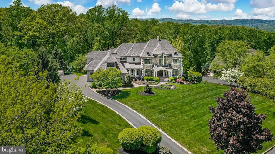 This stunning, custom home, prominently positioned on three acres high atop Saddle Ridge, has breathtaking, long- distance views over Saucon Valley. The remarkable 6,900 square foot home has been totally transformed and expanded by the current owner, with magazine-ready details and impeccable taste. A 2021 infinity pool, patio and deck are enveloped by custom landscaping, manicured drive, perennial gardens and perfect privacy. The stately, stone exterior and custom design are beautiful first impressions of the quality echoed in the home’s interior. Designed by Chuck Harrison, the exterior is reminiscent of the European countryside, and offers a fabulous marriage of design and position.
Natural wood and stone finishes are used exclusively throughout with sumptuous floors of wood, granite, marble and tile. A grand foyer, with an elegantly turned staircase, opens to dining and living rooms, with detailed custom woodwork and fun surprises at every turn. The first floor has vaulted and ten-foot ceilings, walls of Pella true-divided light windows and a handsome library featuring finely crafted millwork. However, it is the gourmet kitchen that will melt your heart, remodeled in 2021 with custom cabinetry, quartz countertops and the finest appliances. Steps away, a sun-filled, domed family room has a fireplace with lapis granite surround and the perfect position, overlooking sunsets and the private acreage beyond. A striking master suite with vaulted ceiling, fireplace and elegant bath is on the second floor. There are nine-foot second floor ceilings, a future elevator closet, four additional bedrooms and a 2017 bonus room designed for family and friends. These more than fun, family accommodations are unexpectedly enhanced by a lavish lower level with recreation room, game room, wet bar, full bath, changing room and a swim against pool in a separate, environmentally controlled room.