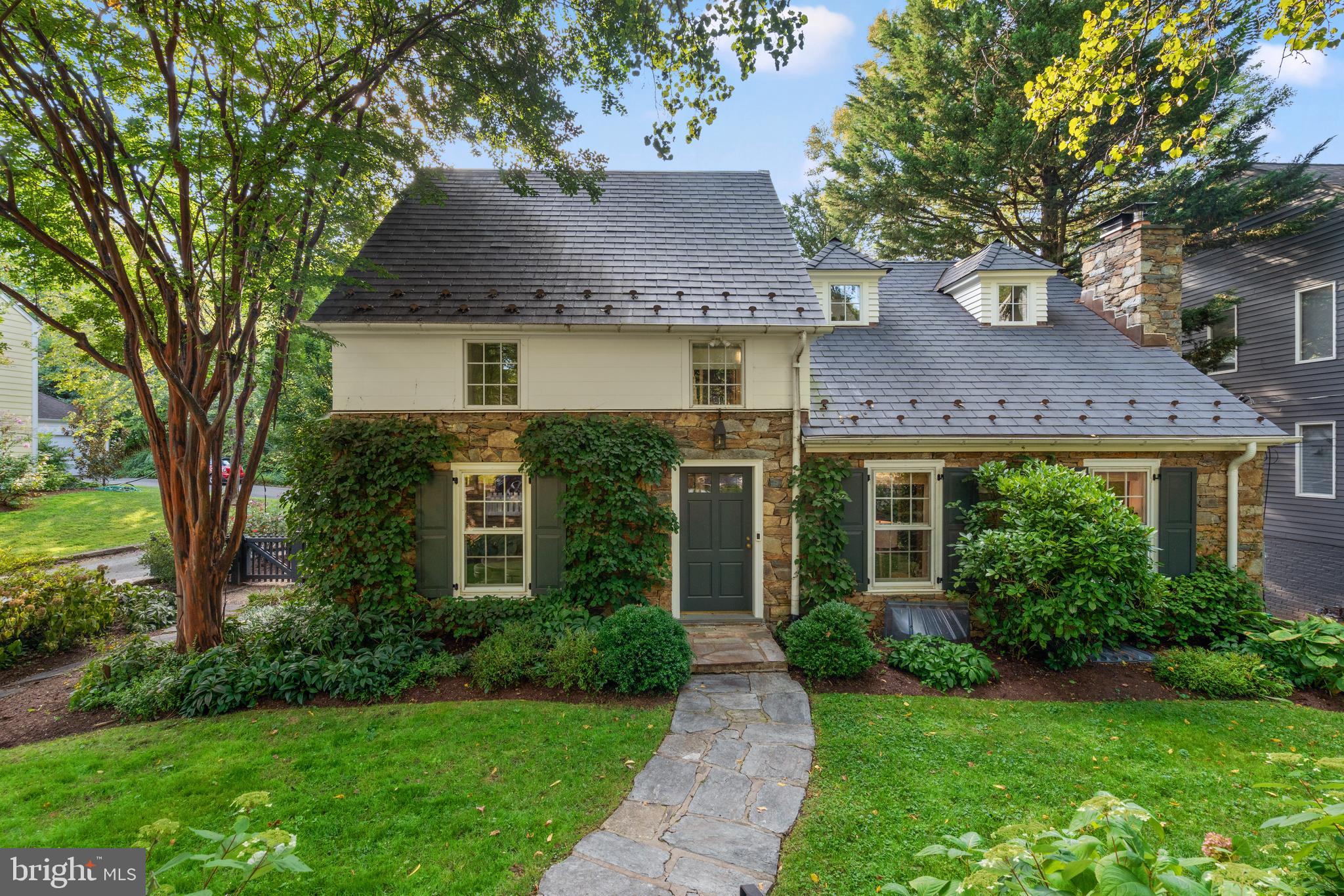 Discover the quintessential charm of this historic stone residence, nestled in the coveted Town of Somerset. Originally built in 1935, this home underwent a significant renovation in 2018 by the esteemed Zantzinger, seamlessly blending timeless character with contemporary living standards. The house retains its original allure while now offering enhanced flow, functionality, and comfort.
Upon entry, you are welcomed into a vaulted living room adorned with a wood-burning fireplace and Urban Electric pendant lights, creating an inviting and warm atmosphere. Adjacent to the living room, a den features custom floating bookshelves and ceiling paneling, ideal for a cozy reading nook, office, or small TV room. The kitchen serves as the heart of the home, seamlessly connecting the dining and living areas to the beautifully designed rear patio through elegant double doors with side lights.
The first floor boasts a spacious family room with a gas fireplace and windows on three sides, offering ample natural light. An adjoining pantry, with its limestone tile floors, built-in shelves, and laundry facilities, includes a full bathroom complete with a tiled shower and a basalt sink.
On the second floor, find two charming bedrooms and a bathroom, alongside a luxurious primary suite featuring a ceiling fan, art lighting, two closets, and a bath adorned with marble and stone tiles. The top floor presents a delightful bedroom with treetop views of the backyard, built-in bookshelves, and a cozy bench seat.
The mature front garden is graced with a heritage crepe myrtle, three varieties of hydrangeas, and a dogwood, while the rear garden features a rose garden and a serene, fenced-in stone patio adorned with perennials, a flowering cherry tree, and a row of American hornbeams. A garage is conveniently accessible via the rear drive.
Recent updates since 2018 include a dual-zone HVAC system, a new roof, new windows, renovated bathrooms, a new pantry, an expanded coat closet, an enlarged third-floor room, and a new rear stone patio. Outside, enjoy proximity to Somerset Elementary School, the beloved Somerset Pool, tennis courts, Capello Park, as well as the Friendship Heights metro, Bethesda, and the Capital Crescent Trail.