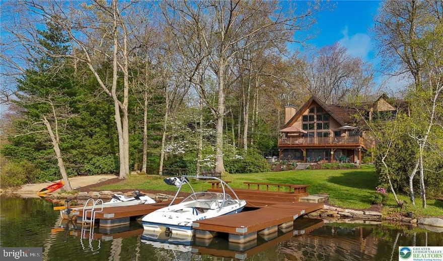 Imagine celebrating each glorious Pennsylvania season from a home that defines idyllic lake life, comprehensively enjoyed from its private beach or sprawling paver patio, the twenty-foot-tall living room windows or the private upper-level sanctuary of the primary bedroom. Approaching from the home’s front, the attention to detail and care are immediately evident in the warm tones and stone accents wisely chosen to harmonize in the lush sylvan surroundings, protected greenbelt area borders the property to one side. The entry porch opens to a lovely foyer, its ceramic tile becoming gleaming hardwoods leading up to the main level’s free-flowing gathering space. The kitchen is open to a gently defined dining room as well as the living room, its wood-beamed, pine tongue and groove cathedral ceilings soaring to a twenty-two-foot peak. Abundant windows overlook the deck, yard, and lake beyond while a wood-burning fireplace offers charm and comfort. A stone fireplace surround with wood accents in trim and railings offer organic touches and, when paired with the floor and ceilings, appropriately hearken the perfect feel of a cozy lakeside cabin. Secluded from the gathering spaces are two well-sized bedrooms, one with a built-in home office workstation and beamed ceiling, the other a beamed, tongue and groove ceiling amplifying its rustic beauty. A main-level full bath is fully updated with a lovely tub-size shower. The main level also boasts a welcome number of closets in the hall and bedrooms.  A staircase leads from living room to the upper level where a generous sitting room loft awaits, overlooking the living room, it is the perfect nook from which to enjoy the soaring windows with their views of the glistening lake. A second, updated full bath accompanies two lovely bedrooms, both taking full advantage of their dormer location to continue the wood ceilings to offer an ideal sylvan sleeping experience. The primary bedroom offers four hundred square feet with the gem in this crown being a large window situated in the dormer allowing for perfect views of the lake and wooded hills to the south; imagine waking to this view every morning and curling up in a comfy chair with your coffee as the first beams of sun glitter on the gentle rippling of Lake Hauto. The primary bedroom also offers two closets, one a generous 9x14 walk-in, as well as a 150sf private home office. The home’s lower level offers abundant entertaining space from its five-hundred square foot L-shaped family room set around a two-hundred square foot second kitchen with laundry facility. An enclosed porch offers access to the yard and paired with the lower level’s utility room, storage space for a multitude of outdoor toys and furniture! Access to the home’s backyard amenities is also found in the main-level composite deck. Sliding glass doors from the living room offer access to this area with ample space for an outdoor living room and outdoor dining room! Stairs lead down to the 858 square foot paver patio which offers a bonus in its regulation, concrete shuffleboard court as well as a corner nook with fire pit, a stone wall offering an attractive border with seating potential. The patio gives way to a lawn gently sloping to the home’s private beach to the right, and three-boat-dock to the left with a lovely gathering space, built in benches an ideal location to enjoy the water’s edge. The lake front of this home is the southernmost point of land extending into Lake Hauto, offering an ideal location to take in the complete scope of its riparian beauty. While Lake Hauto Club does allow for powerboating, jet skis, and similar, this lake side oasis sits within the “no-wake zone” of the lake, offering a more tranquil experience.   Lake Hauto Club amenities include four public beaches with boat docks and pavilions, tennis and pickleball courts, a community gym and library, and of course the 330-acre lake itself.  Situated at the mid-point bet