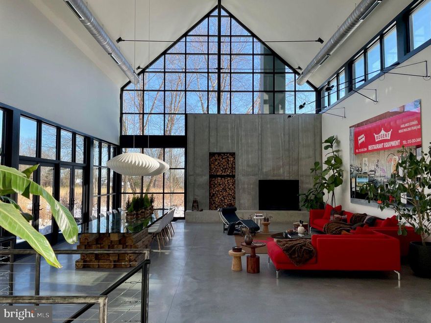 A Published Architectural Masterpiece — The Glass Barn, published in Architectural Record (1988) and reimagined in 2020, The Glass Barn is a landmark of modern design that marries dramatic architecture with effortless livability.  Designed by Richard Olcott and Todd Schleimann of Polshek & Partners, this striking residence is defined by 28-foot soaring ceilings, expansive open spaces, and walls of glass that frame the surrounding landscape as living art. At the heart of the home, the great room showcases a floor-to-ceiling concrete wood-burning fireplace, polished concrete radiant-heat floors with reclaimed hardwood accents. The expansive chef’s kitchen is both functional and dramatic, with soapstone countertops, diamond-plate custom steel cabinetry, professional-grade appliances, and a seating area with a wood burning fireplace. A 1,200-bottle climate-controlled glass wine room completes the entertaining core.
The primary suite is a sanctuary unto itself, featuring a circular glass-walled sitting room with a suspended fireplace, spa-like bath with skylit stone shower, and a boutique like dressing room. Additional highlights of the home include a circular-walled library, a studio, five bedrooms, three and a half baths, a full-floor recreation room, a panic room and an attached 3 car garage. Set on 6.3 acres of rolling meadow and mature trees, the property is as serene as it is private. A two-acre wildflower field with meandering paths provides a changing canvas with each season, enhanced by professional landscaping, lighting and irrigation. The resort-caliber amenities rival those of a private club: Black-bottom heated pool with sun shelf & spa, pickleball/platform tennis court & bocce court, heated commercial glass greenhouse; a year-round grand entertaining space with seating for 20 and dual wood burning fireplaces, expansive lawns, multiple outdoor dining areas, and a large motor court for guest parking. The Glass Barn is more than a residence — it is a published work of art, a stage for entertaining, and a retreat for ultimate privacy. An architectural icon that continues to evolve without losing its original vision.