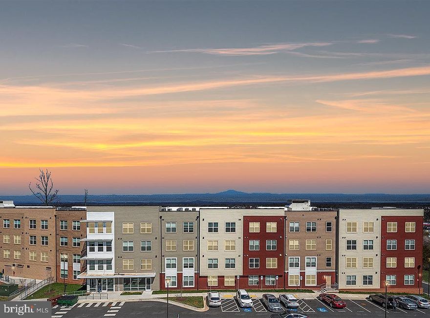 Why wait for new construction when this condo is ready for you to move in (owner never officially moved in)! Experience luxury living at its finest in this brand new, top floor, corner unit boasting breathtaking sunset views of the distant Catoctin and Sugarloaf mountains. Designed with a bank of windows, this residence offers vistas from every front corner for the condo, ensuring a picturesque backdrop whether you're cooking, dining, relaxing, or entertaining.  The open concept layout seamlessly connects the kitchen, dining area, and living room, creating an ideal space for gatherings and everyday living. The gorgeous kitchen features white quartz countertops, stainless steel appliances, a spacious pantry, and an inviting island perfect for entertaining. The main bedroom has ample space with a walk-in closet and private bath, while the second bedroom at the opposite end of the condo offers privacy and convenience with its own hall bathroom.  Step outside to relax and unwind on your private composite deck.  Modern and safety amenities include elevator access, Ecobee thermostat, front lobby security system that can be monitored on your phone, Refuge Room in case of fire, and card entry for your garage parking.  Take advantage of the community's half basketball court, pickleball court, tot lot and refreshing pool, just steps away from your front lobby door. Not only does this condominium offer a luxurious living space, but it also provides easy access to a plethora of entertainment options and recreational activities, ensuring there's something for everyone to enjoy nearby.  Walking enthusiasts will appreciate the proximity to the nearby Harris Teeter shopping center and a variety of restaurants. Target and Costco are also conveniently located just around the corner. For those seeking excitement, explore entertainment options at Top Golf, iFLY indoor skydiving, or enjoy outdoor activities at Claude Moore or the indoor facility that  includes indoor pool, basketball courts & gym. Fulfill your shopping desires at Dulles Mall, Reston Town Center, and Tysons Corner, where you'll find an array of stores catering to every taste and style. Nature lovers can immerse themselves in the beauty of Great Falls Park, where hiking trails and stunning waterfalls await. Close proximity to commuter Route 7 and 286 ensures easy access to transportation hubs and major thoroughfares.