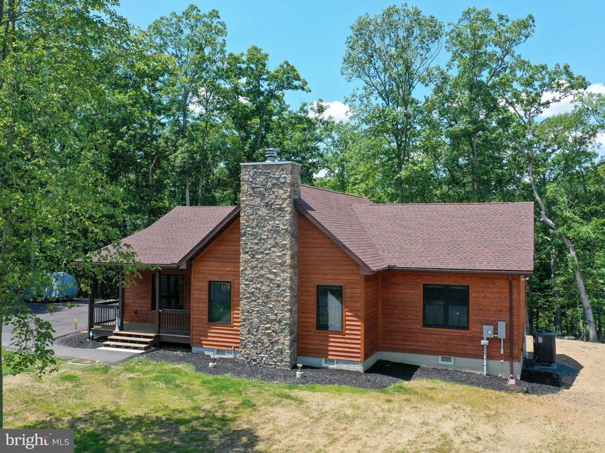 Get ready to be WOWED! Built only one year ago, this upscale cabin in the woods sits on over 2 wooded acres and is expertly crafted for maximum enjoyment and comfort. The inviting exterior features cedar siding, a newly paved driveway, a covered front porch and side entry, and a private back deck with an accessible ramp. Inside this stylish 3-bedroom rancher, you’ll find an open floor plan with gorgeous vaulted wood ceilings with wood beam accents, a striking stone-cladded, floor-to-ceiling wood-burning fireplace, and durable LVP flooring throughout. The kitchen features granite counters, bar seating, a large built-in pantry, and stainless steel appliances. Other standout features include a tray wood ceiling in the primary bedroom, tile floors & showers in both bathrooms, additional wood ceiling and wall accents, and artistic accent lighting. This home is well-built with interior sound barrier insulation and a spacious, well-lit, 6' walk-in crawl space with concrete floor affording a plethora of storage options. The side entry leads into a mud/laundry room for added convenience. Get to downtown Berkeley Springs in 10 minutes, Cacapon State Park in 20 minutes, and the metro areas of Winchester, VA or Martinsburg, WV in under 45 minutes. The well-appointed Kesecker Knoll community provides the seclusion of living in the woods while being close enough to modern conveniences.
