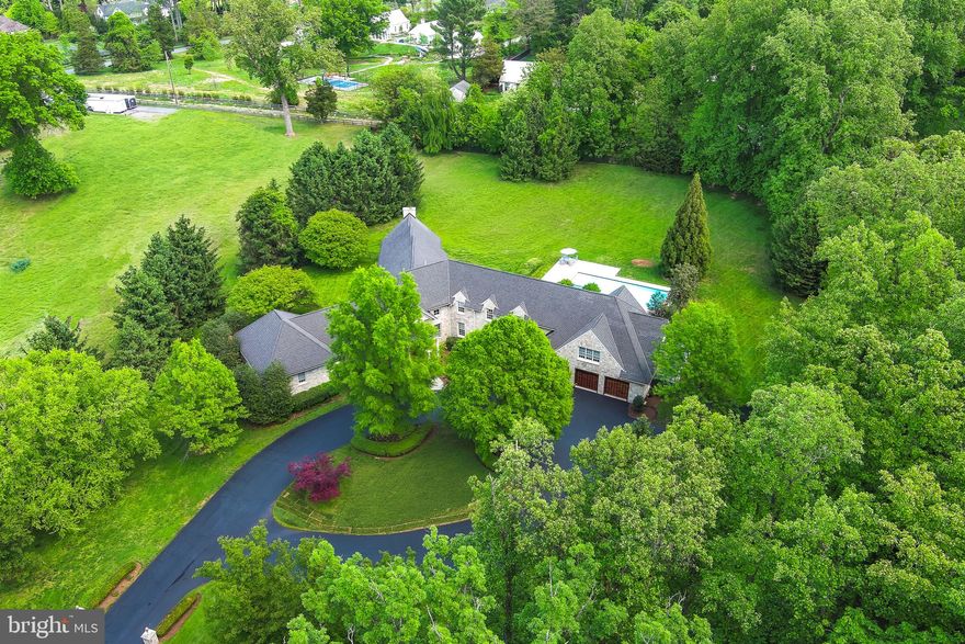 Rarely does an estate of this magnitude and distinguished design become available in the heart of Potomac. Set back behind a sweeping circular driveway on a majestic 2.5-acre level lot, this residence offers a "country-quiet" atmosphere just minutes from Potomac Village. The grounds are a true private oasis, anchored by an expansive in-ground pool and veranda designed for grand-scale outdoor entertaining. For the car enthusiast or the active household, the property features a rare 6-car garage, providing ample space for a collection or hobbyist needs.  The interior experience begins in a breathtaking grand entry featuring dual staircases that lead to a sophisticated gallery. The main level is designed for both formal elegance and daily comfort, boasting a seamless flow between the large dining room and the living room, which are separated by a perfectly positioned private office. Two powder rooms on this level serve guests, while a dedicated back staircase off the kitchen ensures easy movement throughout the home.  The main-level primary wing is a masterclass in luxury, offering a true sanctuary with "his and hers" separate bathrooms and individual dressing areas. At the heart of the home, the kitchen and sun-drenched family room serve as the central hub, featuring large windows and direct access to the outdoor patio and pool. Upstairs, the accommodations remain equally impressive with four additional bedrooms, each featuring its own private en-suite bathroom. One of these upper-level suites is particularly expansive, including its own private sitting room—ideal for a second primary, guest wing, or au pair suite.  The lower level is a world of its own, accessible by two separate staircases located at the foyer and off the kitchen. This sprawling lower level is fully equipped for recreation and hosting, featuring a large rec room, a dedicated home theater, and a second kitchen. This level is completed by a bonus room, a powder room, a full laundry suite, and two substantial storage rooms. Whether you are looking to renovate this substantial floor plan into a modern masterpiece or enjoy the classic proportions of a true Potomac estate, 9001 Persimmon Tree Road represents a premier investment in lifestyle and location.