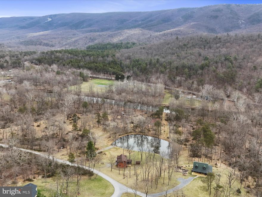 Experience the ultimate lifestyle in this custom-built LOG HOME, crafted with superior quality and impeccable attention to detail. Situated on a 5.21-acre lot, this home boasts 288.34 FEET OF WATERFRONT ON THE CACAPON RIVER, complete with a LARGE, STOCKED POND. Enjoy endless outdoor activities—whether it’s fishing, swimming, or tubing—right in your backyard. The lot is mostly cleared around the home, with wooded areas along the river, ensuring privacy and a natural setting. The house is out of the floodplain, providing peace of mind. Inside, you'll be greeted by a spacious great room featuring soaring vaulted ceilings with exposed beams and pine planking, creating a warm, rustic atmosphere. Two sliding glass doors in the dining and living rooms frame spectacular views of the pond, and double doors lead directly to the deck for easy access to the water. The living room is highlighted by a beautiful stone fireplace, perfect for cozy evenings. Natural light pours in throughout the home, enhancing the open, airy feel. The gourmet kitchen is a chef’s dream with expansive granite countertops and a breakfast bar for casual dining.  Step out to the screened-in porch, an ideal spot for grilling or enjoying your morning coffee.
The main level offers a primary bedroom and a full bathroom for convenience. Upstairs, the loft overlooks the great room and offers sweeping views of the pond. This versatile space could be used as a bedroom, den, office, or studio. Two additional bedrooms with cathedral ceilings and another full bathroom complete the upper level. The unfinished basement provides ample potential for customization to suit your needs. This property is located in the prestigious, gated community of River Ridge, just outside Berkeley Springs, WV. Enjoy the area's renowned warm mineral waters, relax at local spas, dine at award-winning restaurants, and explore nearby hiking, biking, horseback riding, and golf opportunities.
A piece of local history, this home was once owned by the College of Medicine at the University of Cincinnati and the well-known NBC newscaster, Jim Vance. A truly one-of-a-kind property—don’t miss your chance to see it for yourself!