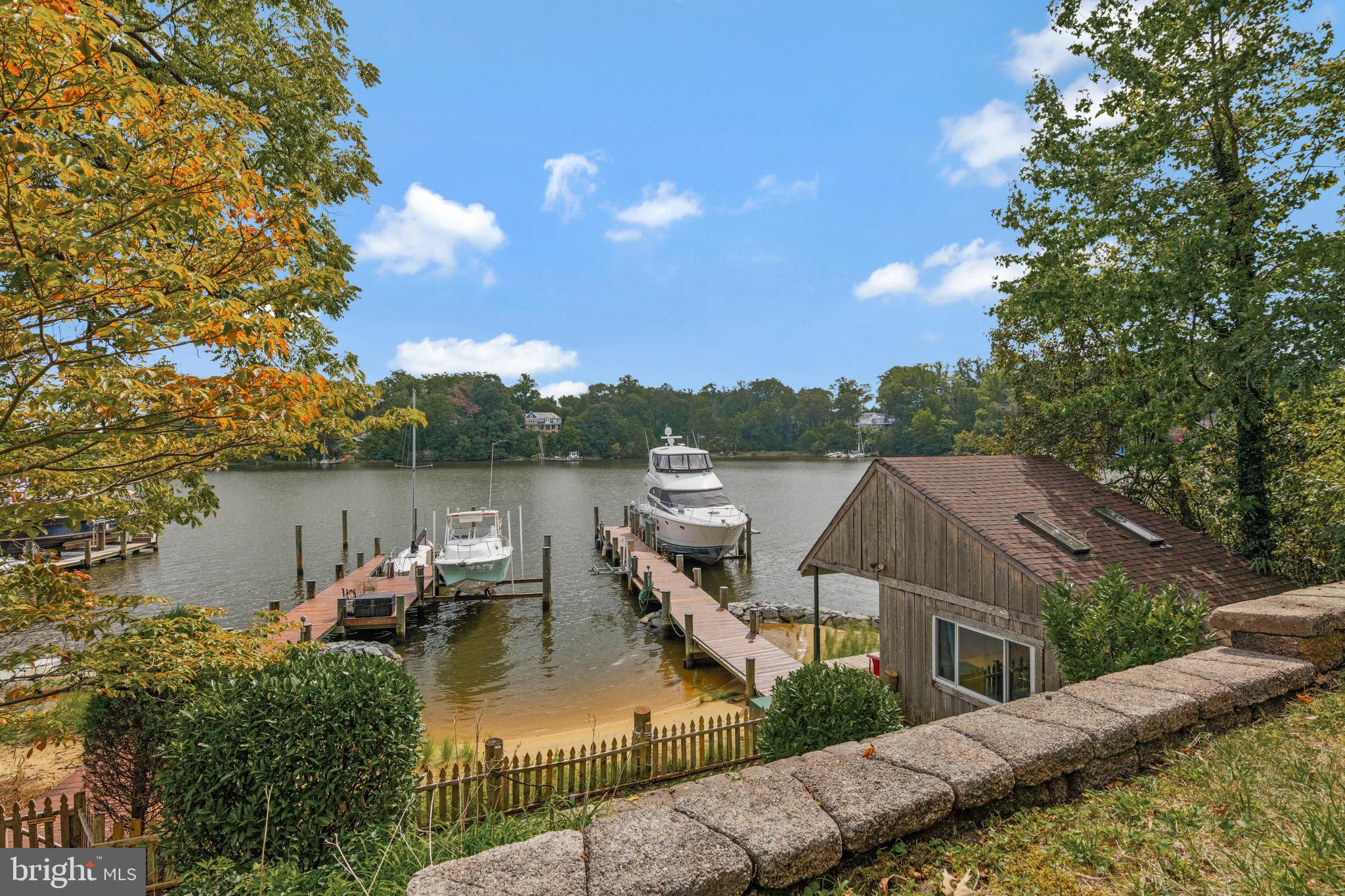$200K PRICE REDUCTION!! Perfectly positioned atop a professionally terraced and landscaped hillside with unsurpassed, panoramic views of Beards Creek and across the South River, this timeless Tudor style home built in 1933 effortlessly blends timeless architecture with high-end modern upgrades, and from this elevated vantage point nearly every window frames the serene, panoramic vistas below. The waterfront showcases a professionally installed living shoreline, completed in partnership with AA County, designed to reduce erosion, preserving rare sandy beach and enhancing coastal habitats. There are two piers, total of five deep water slips, both piers with lifts, electric, and bubbler systems, along with a rare, irreplaceable gem, a vintage cottage that sits directly at water’s edge, complete with front porch and swing. As you step inside the home, you’ll immediately be drawn to the intricate details of the original architecture, perfectly complemented by contemporary updates. Stained glass windows cast colorful light across the rooms, wood beams grace the ceilings, and arched doorways, vintage solid wood doors and trim adapted from a church nearby, and durable slate roof all tell a story. The remodeled kitchen is outfitted with sleek, top of the line appliances, rich wood cabinetry, granite countertops and a large center island. A cozy gas fireplace adds warmth and ambiance. The living area is a blend of openness and warmth, designed to take full advantage of its stunning waterfront setting with vaulted, wood-paneled ceilings soar above, accentuated by exposed beams that add a sense of rustic elegance and architectural depth. Multiple cottage style windows with stained glass windows across the top seamlessly connect the indoors to the expansive deck outside that stretches across the entire front of the home. Just off the living area is a dining room and inviting space with a pellet stove with a beautifully carved wood surround. The bedroom wing on this main level features two bedrooms and two full baths with showers, along with a laundry room. Venturing to the upper level, an open two story ceiling and skylights provide an open and bright space, with a quiet workspace or peaceful nook offering views of the ever changing waterfront scenery beyond. The luxurious owner’s suite completes the upper level, offering a private retreat with comfort and style. At the center of the suite is wood burning fireplace with wood mantel surround and french doors that open into the private balcony with sweeping views. The suite also includes an incredible en-suite bath designed with both elegance and function in mind. A large walk-in shower with custom tile work and glass enclosure creates a spa-like experience, while thoughtfully designed fixtures and finishes add a touch of sophistication. A large shed complete with electric front porch sits at the top of the hill. The South River Heights community is a Special Community Benefit District, and community offers a pier with slips for lease, pavilion, kayak launch and storage, and fire pit!