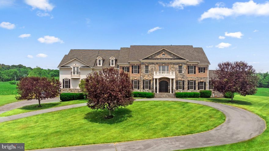 Welcome to this extraordinary custom-built stone estate, situated on over five private acres and offering an impressive 12,166 square feet of luxurious living space across four impeccably finished levels. Designed for grand-scale entertaining and refined everyday living, this remarkable residence showcases wood flooring on all three above-grade levels, complementing the home’s timeless craftsmanship and architectural elegance. With seven bedrooms—each with its own private bath—seven full baths, and two powder rooms, comfort and privacy abound. Five fireplaces, a whole-home entertainment sound system, and exceptional millwork further elevate the living experience. Car enthusiasts will appreciate the extraordinary 8-car, 42’ x 45’ garage featuring elevated ceilings, a car storage lift, and truly a rare offering. A dramatic two-story foyer with a graceful curved staircase sets the tone for the grandeur within. The foyer is flanked by an immense formal dining room and an elegant living room with a gas fireplace and arched openings. Beyond, the magnificent great room impresses with a soaring stone floor-to-ceiling fireplace and a wall of windows providing deck access and sweeping views. The gourmet kitchen is nothing short of spectacular, complemented by an oversized breakfast room. Additional main-level highlights include a distinguished formal library, a stunning sunroom with cathedral ceilings and abundant natural light, a mudroom, and two conveniently located powder rooms. Upstairs, the primary suite is a private sanctuary featuring a sitting room with a see-through fireplace, a wet bar with refrigerator beneath granite counters, a 16’ x 16’ fitness room with balcony access, and a lavish primary bath with dual lavatories. The suite is completed by a private second laundry room, exquisite millwork, and an extraordinary 25’ x 15’ custom closet space. The regal landing with iron rod railings overlooks both the grand foyer and great room below. Four additional expansive en-suite bedrooms—one featuring a stone fireplace—and a second laundry room complete this level. The lower level spares no expense and is designed for exceptional entertaining and relaxation, featuring a recreation room with a stone fireplace, a game room, an office/den, a full bath, a media room, and a stunning bar with expansive granite counters, a sink, a refrigerator, rich wood cabinetry, and seating for six. Walk-up stairs provide convenient access to the rear grounds. No detail has been overlooked in this extraordinary estate—a masterful blend of luxury, comfort, and architectural distinction.