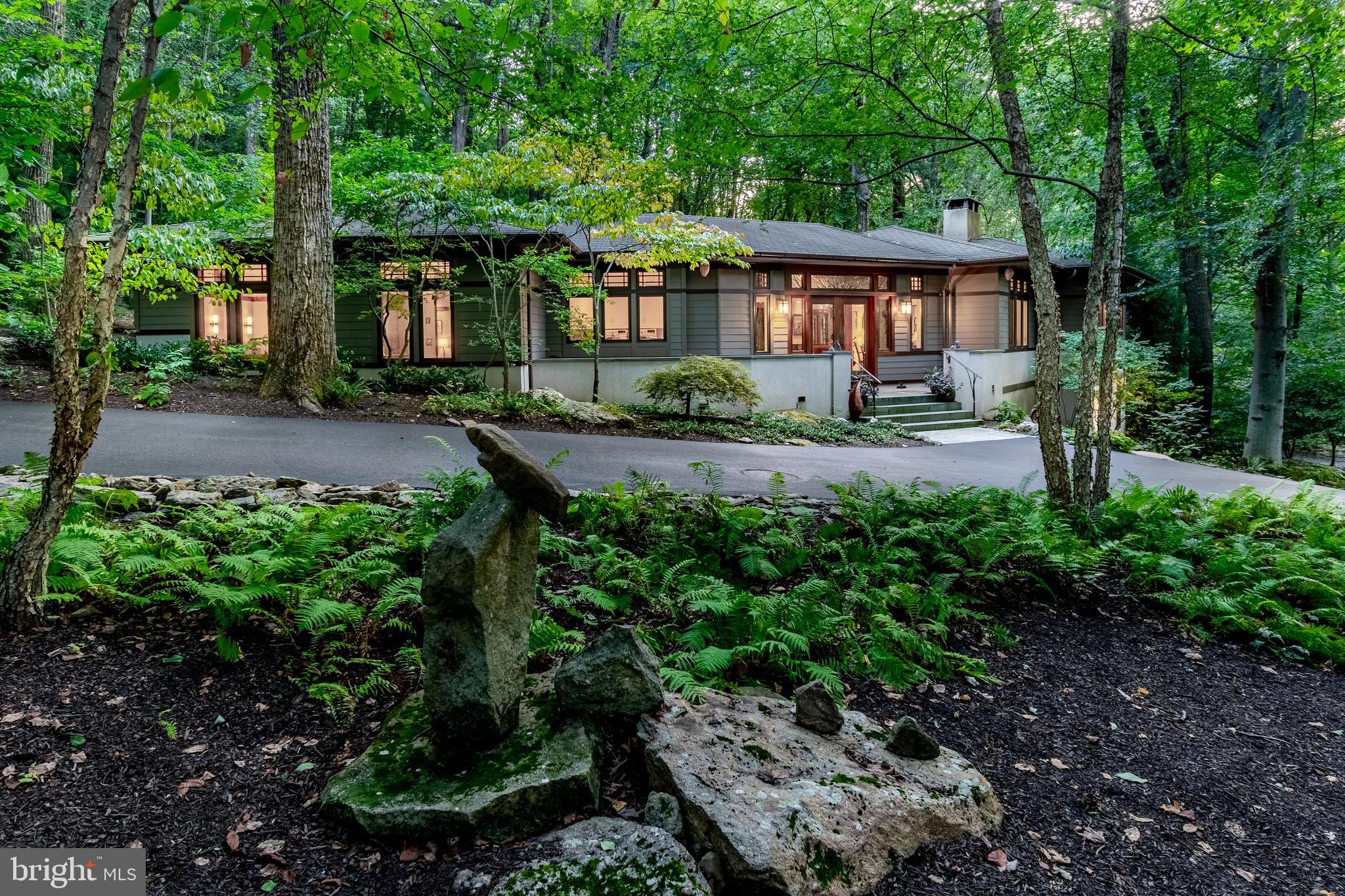 Gracefully situated along a wooded hillside, this Prairie-inspired home is a masterclass in thoughtful design and connection to surroundings. Set on 2.5 acres, the AIA Residence Award-winning house curves gently with the land, maximizing light, space for art, and privacy while honoring the site’s natural contours. Inside, the main living area is expansive and warm, with 11-foot ceilings, large windows, and transoms that invite natural light from every direction. The color palette, drawn from the surrounding woods, features amber tones and soft green grays that ground the home in its landscape. Temperature is controlled by heat pumps, with geothermal adding radiant comfort to the main floor. The custom kitchen is as beautiful as it is functional, with hand-crafted alder cabinetry, vertically grained panels, and an extraordinary earth-tone granite countertop that reflects the surrounding landscape. A six-burner stove, marble baking station, dual sinks, convection and regular oven, and integrated pantry create a space designed for enthusiastic cooking and baking. The beautifully figured cabinets flow seamlessly into the dining area, where a quiet corner window seat and room for all your dishware continue the home’s thoughtful details. Throughout the house, design elements emphasize connection over separation. Tile gently rolls into wood, beams stretch into walls, and ceilings wrap softly down to the beltline so it floats overhead. A fireplace with a custom Nakashima free edge mantle having unique branches motif, a hidden inscription, a custom picture hanging system, leaded glass, and handcrafted railings all speak to the home's artistry and intention. Pocket doors allow wall space for art and a smart layout encourages flow. Art is integrated into the very structure with small niches that hold original pieces created specifically for the home, with many noted Bucks County Artists represented. The main floor houses the primary suite, office, and living spaces. The Master suite includes generous closets, a serene bathroom with dual sinks, an ample dressing area, and a storage/laundry room. All designed for comfort and practicality. The lower level includes a guest suite of rooms with a gas fireplace, full bath, second laundry, and massive storage space, all with a separate entrance. Above the three-car garage, a 1000 sf studio offers bright, open space for creative work, complete with skylights, a mural wall, work sink, half bath, wood stove, and a large rear door for moving oversized pieces. Downstairs includes a generous workshop. Every inch of this award-winning home reflects a clear vision: graceful, grounded, and designed to be lived in beautifully and comfortably, with sustainability, quality and elegance working quietly behind the scenes.