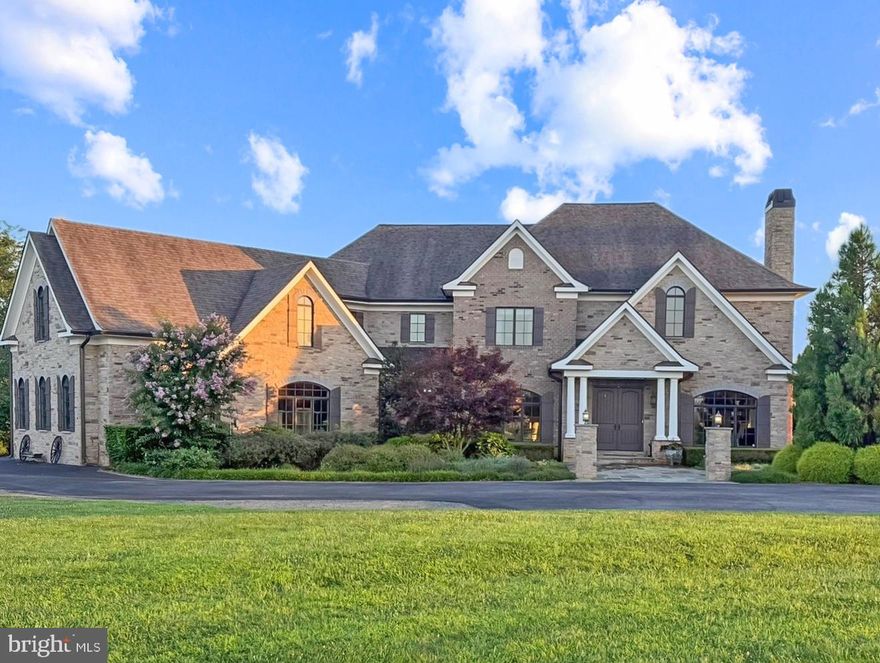This romantic French Country revival, set within coveted Lee’s Crossing, unfolds gracefully from its bucolic surroundings, where provincial architecture is framed by flowering trees and seasonal blooms. Built in 2017, the home captivates with the chic sensibility of nearby Lucketts shops, showcasing approximately 6,000 square feet of open living finished with wide-plank hardwood floors, tailored built-ins, and elevated ceiling heights. Delicate chandeliers gently punctuate thoughtfully crafted spaces for gathering, dining, and retreating, while expansive windows frame pastoral vistas and sweeping sunset views like living works of art. In the airy chef’s kitchen, professional-grade appliances pair beautifully with cloud-hued cabinetry, stone countertops, and a nostalgic farmhouse sink. From the island, add the finishing touches to meals as guests select a bottle of local vino from the wine refrigerator. Outdoors, the covered grill space invites relaxed game nights and late-evening conversations around the firepit, with s’mores-ready serveware close at hand. Overlooking 13.8 sweeping acres, the landscape inspires visions of a future barn, a summer-ready pool, or open lawn games with a four-legged companion. Perhaps the home’s most striking feature, the central staircase serves as both anchor and destination, leading to restful reading nooks and casually sophisticated spaces designed to tuck away life’s essentials. Five sun-filled bedrooms each connect to high-end baths featuring rain showers, refined hardware, and serene spa-like palettes. A main-level suite comfortably accommodates long-term guests, while upstairs, the owner’s retreat offers a wet bar, dual custom dressing closets, and an indulgent soaking space designed for unwinding. Effortlessly impressive, the upper level also reveals a creative, popcorn-perfect bonus room, alongside a three-car garage and a thoughtfully designed mudroom finished with herringbone tile—setting the tone for cheerful departures and everyday adventures. Just moments from neighborhood horse trails, this exceptional home is surrounded by rural beauty while remaining conveniently close to bustling Leesburg, charming Lucketts, local farmers markets, and all that greater Loudoun County has to offer.