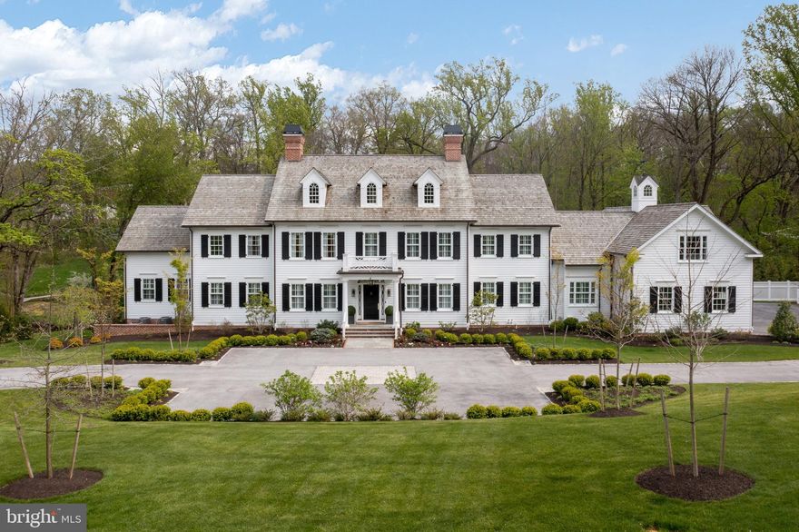 Every day feels like a vacation when you come home to this impressive 2019 E.B. Mahoney home on one of the most coveted tree-lined streets in Bryn Mawr. With two parcels totaling 2.89 acres, and four levels of living space plus an outdoor room, this 12,253-sf custom residence offers all the room you need, the privacy you crave and an ideal location in the coveted Radnor School District less than 3 miles from the Bryn Mawr and Villanova train stations.
Inside and out, you’ll find thoughtful design and exceptional features for ease of living—like a mudroom elevator that services three floors, a whole-house Lutron lighting system and custom built-ins throughout. From hardwood and tile floors, high ceilings, stunning wallpaper and millwork throughout, you’re surrounded by luxury. Fully decorated by Sarah Wolfington of Wolfington Interiors, this home is both impressive and welcoming.
The main level features a huge great room that opens to the outdoor room, and to an intimate bar room with wet bar, fridge and spiral staircase to the wine cellar. A spacious kitchen boasts a 13-ft-by 4-ft island, triple-thick quartz countertops, 6-burner Lacanche French range, 2 Bosch dishwashers, 2 Sub-Zero refrigerator/freezers and a full-size beverage refrigerator. You’ll appreciate both the desk alcove and the pantry/auxiliary kitchen with Wolf stove, plus generous storage and countertops. The light-filled dining/breakfast room opens to the outside room through French doors.
Also on the main floor, the primary bedroom suite is the perfect retreat, with custom remote-controlled window blinds, vaulted ceiling, en suite bathroom with 2 vanities, 2 water closets and a separate room with shower and soaking tub. Two walk-in closet rooms feature custom cabinetry, shelving,
shoe and handbag storage. One has 2 islands with marble countertops, a small refrigerator, a make-up table and a dedicated space for a safe. The suite is just steps from a discrete staircase offering quick access to 2 children’s rooms with shared Jack-and-Jill bathroom and separate vanities. Upper level 1 also has 3 other bedrooms, including a spacious in-law suite, all with walk-in closets, high ceilings and en suite baths. A 2nd laundry on this level adds convenience, and a reading room/minstrel’s gallery with custom trim work overlooking the foyer provides a quiet escape. On the 2nd upper level is a large finished game room with window seats and a rough plumb full bath that you can finish to suit your style.
The finished lower level provides a great space to work and play. Off the extra-wide hallway, an office with custom tray lighting, built-in lacquered cabinets with high-end hardware, hardwood floors and decorator wallpaper opens to the outside patio and yard. A studio with closets, a mirrored wall and ballet barre—perfect for dance, yoga or a home gym—also opens to the outside. A golf simulator room with special flooring and sink, a climate-controlled wine cellar with extensive built-in storage, a bonus family room,
and a full bath with sauna and built-in linen closet add to the home’s resort-like feel.
With nearly 3 acres and an in-ground pool and spa, this property offers a great outdoor lifestyle. Overlooking the pool, patio, trees and the Kirk’s Run creek in your yard, an outdoor room with a fan and heaters in the vaulted shiplap ceiling offers year-round enjoyment, thanks to a large brick surround with fireplace and TV, built-in speakers, and a built-in grill a few steps away. It’s easily accessible from the family and breakfast/dining rooms. You’ll spend a lot of time around the fenced-in pool, swimming or enjoying the gorgeous tile, landscaping and hardscaping. The main-level mudroom, with shiplap walls and storage cubbies, a full bathroom and a  laundry room with deep farm sink and a back stairway all make poolside
time easy. An oversized 4-car garage with extra-high doors, epoxy floors and GarageTek storage system has brick stairs to the house.