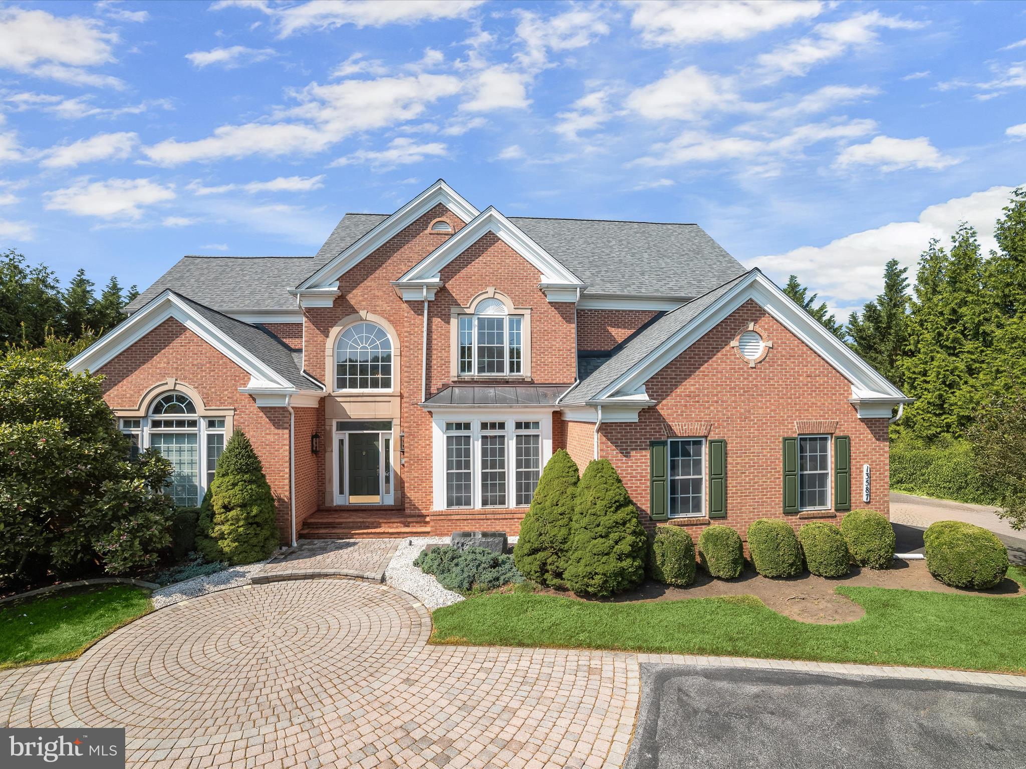 This exquisite brick estate, maintained by its original owners, offers more than 7,000 square feet across three finished levels, all nestled on nearly an acre of lush, private land. Blending timeless craftsmanship with luxurious amenities, the home presents a thoughtful balance of grand entertaining spaces and tranquil private quarters. With custom details, soaring ceilings, multiple fireplaces, a main-level primary suite, roof replaced in 2023, and even an interior sauna, this residence is as impressive as it is inviting. A stately circular driveway with a paver-stone approach welcomes you to the front entrance. Inside, the two-story foyer sets the tone with gleaming marble floors and elegant picture frame molding. To the right, the formal dining room mirrors these finishes and adds crown molding for a refined touch. To the left, a distinguished home office features a fireplace flanked by built-in bookcases and a striking coffered ceiling, ideal for work or study. At the heart of the home is the magnificent great room, where a soaring two-story ceiling and a wall of windows flood the space with natural light. An atrium door, framed by sidelights and topped with clerestory windows, opens to the rear deck, seamlessly connecting indoor and outdoor living. Anchored by a cozy fireplace, this room gives access into the open-concept kitchen, breakfast area, and family room, creating a unique layout perfect for both everyday life and elevated entertaining. The kitchen features 42-inch cabinetry with display space, granite counters, GE Profile stainless steel appliances including a gas cooktop and double wall ovens, a walk-in pantry, and a convenient breakfast bar. The adjoining family and breakfast rooms share a dual-sided fireplace with the great room and have a vaulted ceiling, offering another warm and welcoming gathering space. A butler’s pantry connects the kitchen to the formal dining room, and nearby, the laundry room and access to the three-car side-loading garage offer everyday functionality. The main-level primary suite is a luxurious retreat with double door entry, rich hardwood flooring, picture frame molding, a tray ceiling, and a sunlit bump-out sitting area. The spa-like primary bath includes a double sink vanity, a soaking tub, and a tiled shower with frameless glass, and direct access to two spacious walk-in closets. Upstairs, four generously sized bedrooms each feature walk-in closets. One has a private en-suite bath, and two of the bedrooms are connected by a shared full bath, offering comfort and convenience for family or guests.
The lower level evokes the ambiance of a high-end boutique hotel. Rich wood accents, sconce and pendant lighting, a sleek stone faux fireplace, and multiple sitting areas create an upscale lounge atmosphere with access to the backyard. A raised platform stage is perfect for at-home performances or karaoke nights. The wet bar with seating and a beverage refrigerator anchors the space, and the hardwired sound system enhances the experience. This level also includes a bonus room ideal for exercise or hobbies, a spacious sixth bedroom, and a moody full bath complete with steam shower, heated floor, and a sauna large enough for multiple guests. There is also ample unfinished storage space for seasonal or long-term items. The backyard is a private, park-like escape. A large composite deck overlooks a winding paver walkway, detailed with inset landscaping, a decorative bridge, and mature plantings. This walkway leads to a second patio with a pergola, perfect for outdoor dining or quiet reflection. A six-foot fence encloses most of the backyard while maintaining views of the surrounding landscape and gardens. Additional features include a zoned HVAC, a side-loading three-car garage, and access to highly rated schools. Ideally situated and thoughtfully designed, this exceptional home offers luxury, comfort, and distinction in equal measure.