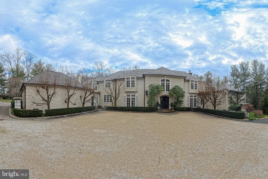 Situated in the heart of Gladwyne, this distinguished residence offers timeless architectural elegance and thoughtfully curated indoor and outdoor living spaces. A grand double-door entry opens to a marble-tiled foyer with soaring ceilings and a sweeping staircase.
The formal living room is highlighted by a dramatic two-story ceiling and expansive floor-to-ceiling windows. A beautifully appointed office features custom wood built-in bookshelves and a fireplace with a striking black marble surround. A second living room, ideally located near the kitchen, is rich in character with cathedral ceilings accented by wood beams, custom wood paneling, detailed crown molding, a fireplace, and a built-in bar alcove, creating an inviting setting for entertaining.
The kitchen is equipped with custom cabinetry, granite countertops, a Dacor gas cooktop, and a         double-door custom Sub-Zero refrigerator. The dining room is a true showpiece, featuring a hand-painted mural ceiling, dual chandeliers, and oversized doors that open to the back patio.
The first-floor primary suite offers a serene retreat with direct backyard access and two ensuite bathrooms, including an updated spa-like bath with a walk-in shower, bench seating, and overhead shower, as well as a second bath with a soaking tub and walk-in shower. Upstairs, six additional bedrooms are complemented by multiple full bathrooms, including several updated baths.
The finished basement adds flexible living space with a recreation area, home gym, and full bath. Outdoor living is elevated by a pavilion-covered patio designed for year-round enjoyment, featuring a substantial brick fireplace with built-in TV, a pool, and professionally landscaped grounds. A three-car garage completes this exceptional Gladwyne offering.