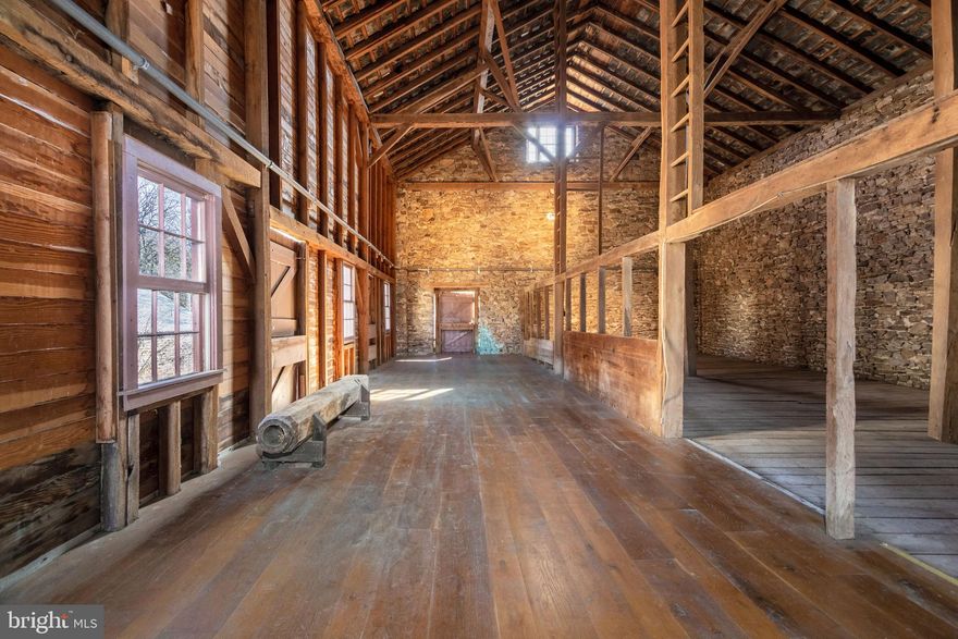 First time offered in nearly 45 years, Esteburne Farm is a quintessential Bucks County estate set on 39 preserved acres along a quiet country road in Solebury Township, New Hope, Pennsylvania. Tucked far from the road in a postcard setting, the property is a remarkable collection of historic stone structures surrounded by rolling pastures, mature trees, and serene countryside. The estate includes a stone main house, stone carriage house, stone garage, stone bank barn, corncrib, equipment shed, and both indoor and outdoor riding arenas, creating an exceptional equestrian compound with timeless character. Built in 1760, the main residence offers four bedrooms, three stone fireplaces, hardwood floors throughout, and beautiful views from every window. Historic details such as high-beamed ceilings, a graceful staircase, and original architectural elements reflect the home’s rich heritage. A large stone patio overlooks the pastoral landscape, while a seasonal stream crosses beneath a charming stone bridge along the drive, adding to the property’s storybook setting. A two-bedroom carriage house, privately situated a comfortable distance from the main residence, provides ideal guest accommodations or a caretaker’s residence. The all-stone bank barn is equally impressive, featuring chestnut floors, 30-foot soaring ceilings, six horse stalls, and a heated woodworking shop. With its dramatic scale and historic character, the barn offers extraordinary potential for a future residence, studio, or event space.