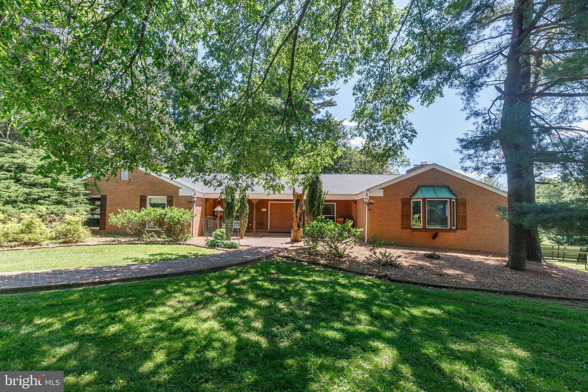 Welcome to 3211 Woodvalley Drive! Featured in House Beautiful Magazine, this one-of-a-kind home has an architectural leading design years ahead of its time. Rarely available five bedroom, four bathroom rancher offering exceptional curb appeal and thoughtful design throughout. Set on just under two beautifully landscaped acres, this property pairs timeless architecture with a warm, functional interior.
Stroll from the driveway to the landscape architected brick walkway and through the comfortable brick and cedar porch. Step inside to a welcoming foyer featuring herringbone brick floor tile and shiplap paneling, lending a subtle mid-century modern touch. The main oak-planked living room is expansive, with vaulted wood-beamed ceilings, a cozy brick fireplace, shiplap accents, recessed lighting, and large sun-filled windows. It flows seamlessly into the dining room, creating an open yet defined space for everyday living and entertaining. Sliding Anderson doors lead to a tranquil, fenced-in back patio with peaceful, private, woodsy views.
At the heart of the home is a gourmet galley-style kitchen designed for both beauty and utility. A custom brick hearth surrounded with a built-in pot rack frames the commercial-grade Wolf gas cooktop, while a Wolf double convection wall oven and stainless steel appliances complete the setup. The exposed brick archway adds a warm, traditional touch, evoking the charm of a European country kitchen.
The main level features a spacious primary suite with an en suite spa bathroom, recently updated with fresh paint, a new double vanity, a freestanding tub, and a stall shower with dual shower heads. A large walk-in closet includes built-in custom shelving. Three additional bedrooms on the main level offer hardwood flooring and ample closet space, supported by two full bathrooms updated with new vanities. A dedicated main-level laundry room adds everyday convenience.
A separate den-style room with herringbone brick floor tile and hardwood ensconced walls and offers additional space for lounging or entertaining, complete with a bar and a second fireplace—featuring bricks sourced from Baltimore’s historic Ford’s Theater. The lower level has been upgraded and includes an exposed brick wall with a wood-burning fireplace, recessed lighting, walk-out access to the backyard, a full bedroom, and an additional full bathroom.
Additional highlights include a newer roof, a two-car detached garage with ten foot garage doors, a geothermal heating system less than a year old, and owned solar panels that have produced negative utility bills during the summer months. Located close to highly rated schools, this property is a rare blend of space, style, and efficiency in a sought-after Stevenson location. Schedule a showing today!
