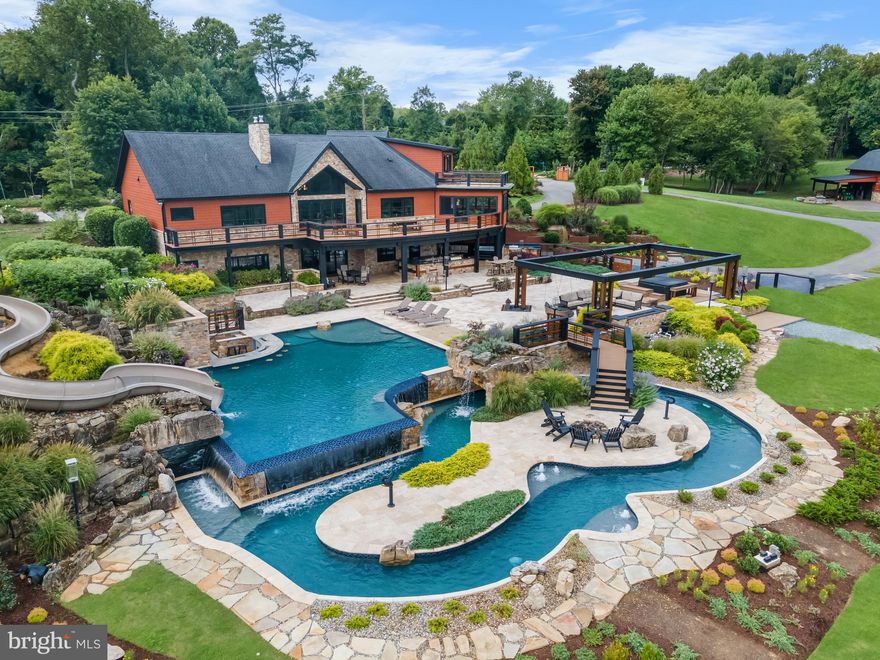 A home for resort-style living and entertaining! This approximately 6,000 sqft home on nearly 10 private acres, surrounded by horse pastures and woods, is ideally situated on prestigious St Stephens Church Road located just minutes from Waugh Chapel, Route 3, and I-97. The quiet location exhibits stunning curb appeal due to recent large-scale architectural landscape renovations to include a new custom entry gate and landscape lighting from street to house for an awe-inspiring approach to your home. Immediately upon entry the high-end updates with form and function abound. A few steps beyond the double door entry opens to a foyer and lodge room that reveals the stunning view of the infinity pool, lazy river, large entertaining area with two outdoor kitchens and bar areas, including a swim up bar. The home is designed to enhance the breathtaking year-round views with oversized Marvin solid cherry custom architectural windows, complemented by interior solid cherry doors and sill candle lights, and large composite deck adjacent to the large screened-in porch. The lodge room features a wood- burning fireplace and stone hearth, complemented by the open floor plan and custom hardwood flooring that extends throughout the entire level. The south-facing chef-style kitchen is highlighted by Wolf and Monogram appliances, a 4-burner gas stove with griddle, induction cooktop, 5ft galley sink, a large island, Italian designer custom wide tiles, full size SubZero fridge and freezer, dual drawer dishwasher, ice machine, drink fridge, and cabinetry. The closely located dining room features a counter and display shelving, including dual wine fridges. A stairway allows upper-level access to an upstairs private apartment/in-law suite with its own balcony and full kitchen. The massive first floor primary wing consists of a bedroom, two walk in closets, bathroom, and office. The bedroom is completed with a sitting area, an electric fireplace, and direct deck access. An exhaustive primary bath and dressing area includes a custom-designed closet and dressing room with hand-laid tiling. The bathroom features a frameless glass dual shower with adjustable jets and Kohler DTV system. The main floor also includes two additional bedrooms with an ensuite, a half-bath, a mud room, and a laundry room. The spacious lower-level includes a movie room, bonus room, bedroom with ensuite, workshop, utility room, and rec room with a wet bar. Slider doors open the lower level to a huge entertainment area and kitchen, featuring drawer freezers, 6ft galley sink, grill, large gas burner for pots, ice machine, and a fridge. The grand entertainment area includes two hot tubs, firebar with a waterfall, dual pools featuring an infinity edge flowing into a lazy river. Walk over the bridge from the main area to the island inside the lazy river, featuring a fire pit and water cannons. The pools feature a total of 2 waterfalls, a slide, swim up bar with fridges, bubblers, and the infinity edge. The entire area enjoys surround sound music and light travertine to limit heat on the pavers in the summer. Following the tunnel through the hill, you’ll find 4 tiers of garden planters and a pool equipment room protecting all pool equipment and providing covered storage for deck furniture. Atop the structure on the hill is a large patio to overlook the entertainment area and property along with the entrance to the slide into the water. Exterior and mechanical updates include exterior soffit and permanent Oelo holiday lighting, rolling door entrance to the basement workshop, redwood Nichiha cement board and stone lend to the rustic mountain architecture, geothermal heating and cooling, full home generator, dual electric car chargers in the garage, a temperature-controlled garage, and a 1000 gallon propane tank. The estate includes a two story 40’x80’ concrete and steel barn, featuring radiant flooring, dedicated backup propane