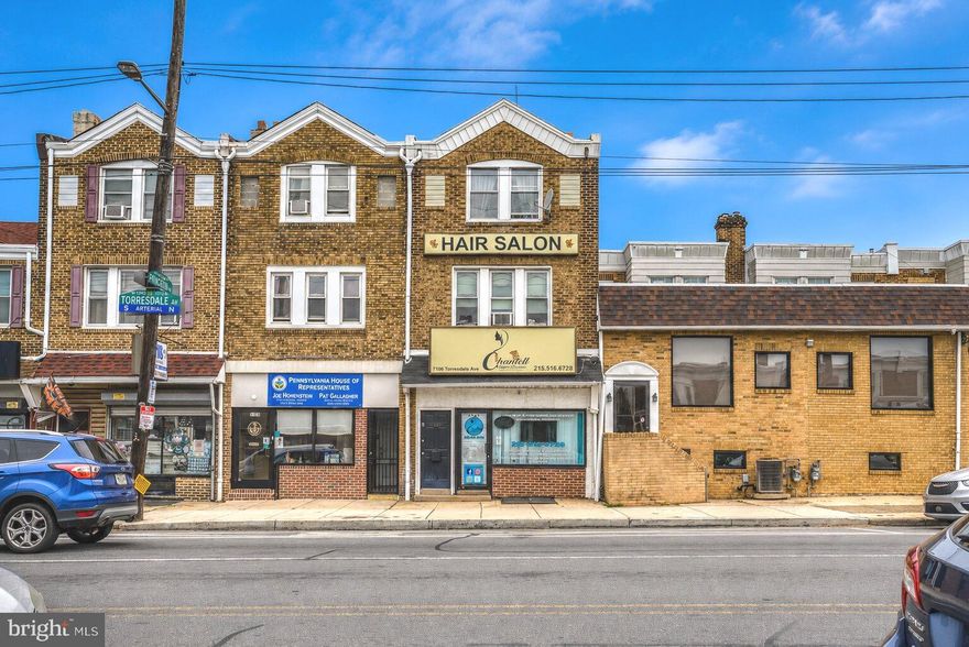 Prime mixed-use investment opportunity located on highly visible Torresdale Avenue in the heart of Tacony. Spanning approximately 2,457 square feet, 7106 Torresdale Avenue features a well-maintained commercial storefront currently operating as a salon along with two residential apartments above, creating multiple streams of income potential for investors or owner-occupants alike. Both apartments are spacious 1-bedroom, 1-bath units offering comfortable layouts, abundant natural light, hardwood flooring, updated kitchens, and classic character throughout.
The commercial space offers excellent street presence, modern finishes, updated flooring, open layout, and outstanding exposure along a busy commercial corridor with consistent vehicle and pedestrian traffic. The property showcases strong curb appeal with its prominent brick façade and recognizable storefront signage while offering flexible income-producing potential in a prime Northeast Philadelphia location. Conveniently located near public transportation, major roadways, shopping, dining, and neighborhood amenities, this versatile mixed-use property presents an exceptional opportunity to add a cash-flowing asset to your investment portfolio.