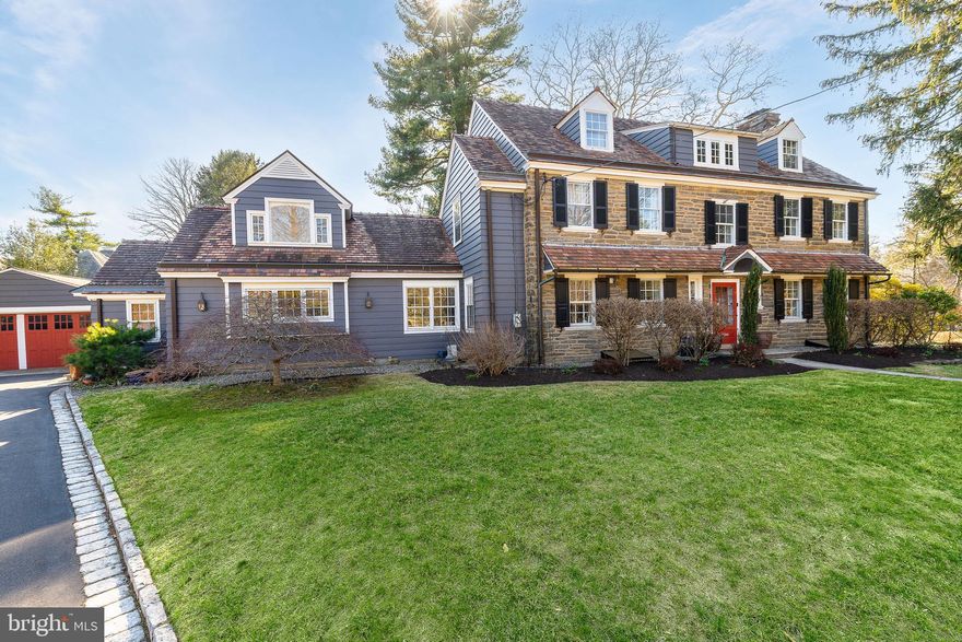 Set on a quiet, elevated lot in one of Wyndmoor’s most desirable locations, this beautifully maintained 1928 center hall stone Colonial offers a rare combination of timeless architecture and thoughtful modern updates. The home blends original character, including detailed millwork, elegant proportions, and a center hall stunning staircase, with meaningful improvements such as zoned heating and central air conditioning. The main level flows effortlessly, featuring a gracious formal living room with fireplace and built-ins, a beautifully proportioned dining room, and a bright enclosed three season room overlooking the garden and yard, creating an ideal space for relaxing or entertaining. The recently updated kitchen features white cabinetry, dark stone counters, a large center island, gas cooking with stainless hood, double wall ovens, and an open, functional layout that flows into a dramatic two story family room with custom built-ins, historic stained glass detail, and direct access to the backyard. A mudroom entry from the driveway connects seamlessly to the home and is complemented by two powder rooms on the first floor. Additional first floor spaces include a spacious laundry room and flexible options for home office or everyday living. The second floor offers a well appointed primary suite with large custom dressing room and a large bath with heated floors, along with two additional large bedrooms and a hall bath, plus a unique loft space overlooking the family room, accessed through a tucked away passage, offering a perfect setting for a reading nook, play space, or quiet retreat. The third floor provides two more bedrooms and a full bath, offering excellent flexibility. The finished lower level adds valuable living space with a recreation area, workout room, workshop, storage, and direct access to the yard. Outside, the property features a patio, level lawn, and thoughtfully designed garden areas including raised beds and a charming spiral garden. A custom oversized four car detached garage with HVAC, Swisstrax flooring, and built-in storage adds versatility for cars, hobbies, or workspace. Located within the highly regarded Springfield Township School District and just minutes from Wyndmoor’s town center, Chestnut Hill, the Wissahickon, and regional rail access to Center City, this is a rare opportunity to own a truly special home.