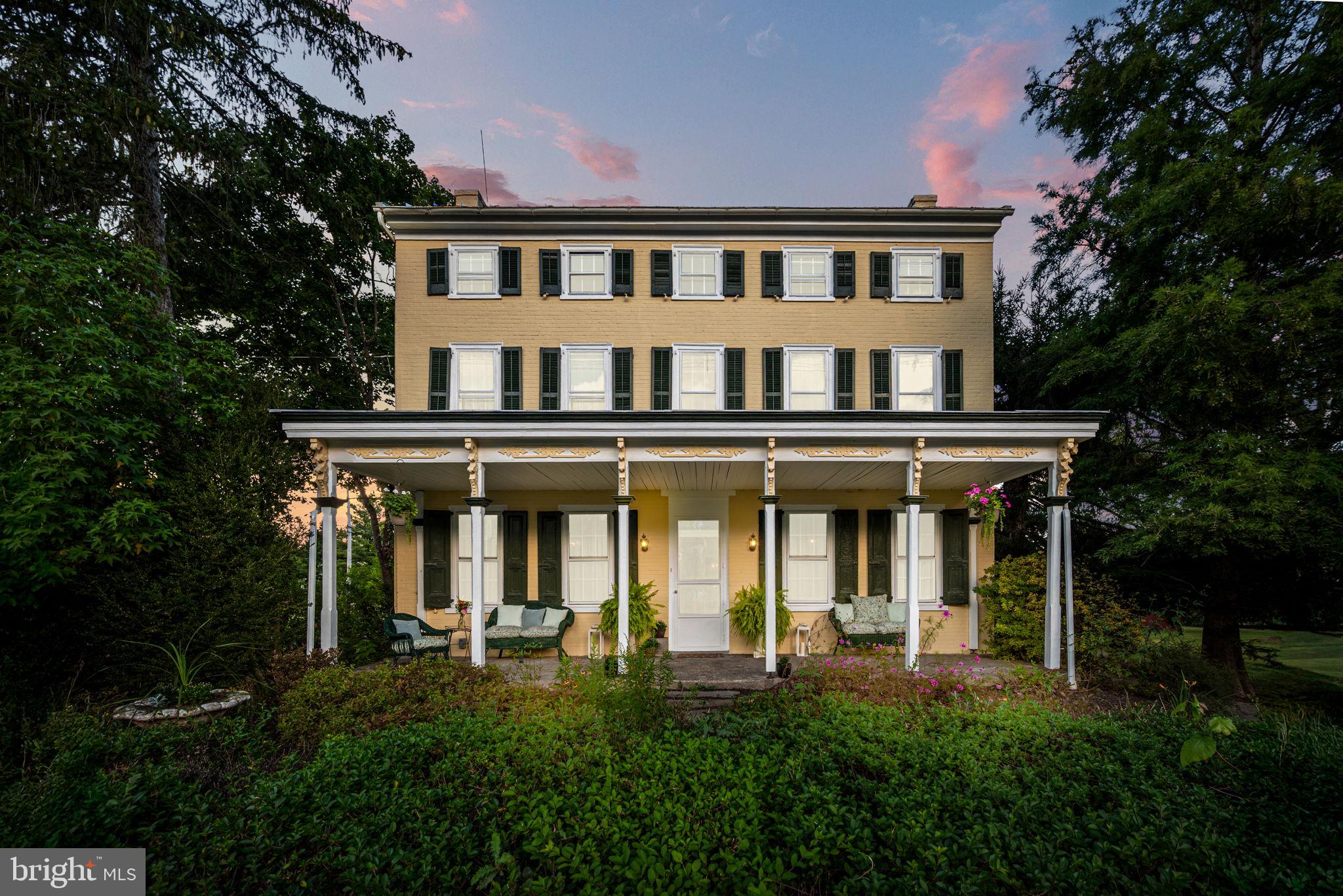 This stately Federal-Colonial style farmhouse blends timeless architecture and country charm. Built in 1796 with two additions (circa 1850 and 1960s) this home offers nearly 3,000 square feet of comfortable living. Original wide-plank wood floors have been beautifully refinished throughout, complemented by 9+ foot ceilings, deep window sills, and rich millwork. A formal dining room sparkles beneath an antique crystal chandelier. The living room is bright and inviting, with a working fireplace, ample tall windows and a decorative ceiling medallion. The kitchen itself is steeped in historic detail, with original milk-painted built-ins, a curved staircase to the primary suite, and the striking walk-in fireplace, which houses the custom-sized oven/range and a working wood stove. It is ready to be reimagined with expanded cabinetry and workspace to suit modern living. Just off the kitchen, the den, once the home’s summer kitchen, remains a rustic retreat, filled with character: rough-hewn wood paneling, exposed ceiling beams and the original fireplace now fitted with a wood stove insert. This inviting space showcases the home’s layered history, where additions and adaptations tell the story of nearly 230 years of evolving use. 5 bedrooms span the home’s upper two levels, with spacious landings that can serve as quiet retreats. Both full bathrooms have been thoughtfully renovated—one located in the hallway with a jetted soaking tub, decorative porcelain sink and tile accents and the other serving the primary suite, which also includes built-in cabinets, a custom glass stall shower, a large walk-in closet, a winding private staircase to the kitchen, and another staircase providing access to the attic. A main level powder room adds convenience. Historical character is found throughout: hand-carved banisters, cobalt blue and stained glass transom windows, and elegant Victorian/Colonial-style millwork. One of the most unique and story-worthy details is etched into the home itself: a hand-lettered quote on the staircase risers reading “We the People… Of the United States” — a poetic nod to the home's revolutionary-era roots. Outdoors, the property offers versatility and potential. Whether you're a homesteader, equestrian, or someone who values open space, the two small barns (15x20 and 16x15) and open pasture provide ample opportunity. A detached 1,500 sq ft garage includes two vehicle bays, a large separate shop room with a wood stove, and a full-height unfinished upper level with windows-perfect for a studio, workshop, or entertainment area. Additional outbuildings include a 9x9 wood shed and an actual working outhouse!
Winding trails weave through the wooded acreage framed by natural vine arches and fruiting grapevines, leading to a small clearing with a sunken fire pit. A well constructed raised bed garden is ready and waiting for a garden to be planted. Perennial gardens and whimsical totem poles carved by a local artist enhance the grounds. One grand sculpture which was created in a tree stump stays with the property. Porches and patios are perfectly placed for relaxing and enjoying the nearly 7 acres. Modern upgrades enhance the rural lifestyle: a solar energy system keeps electric bills at zero, feeding a Tesla Powerwall in the basement that powers the essentials during outages. Three water sources serve the property: a deep well is the primary source of water but there is also a cistern and a shallow well with a hand pump. A spring-fed cold pond in the basement offers a preserved feature of early American life and is perfect for keeping bottles chilled while entertaining. Convenient location offers countless amenities including a Green Lane Park boat launch site 1 mile away. The current owners have meticulously maintained, improved, and preserved the home and its grounds, and most of all, cherished the life it offers. Now, they are excited to pass the keys to the next stewards of this truly special property.