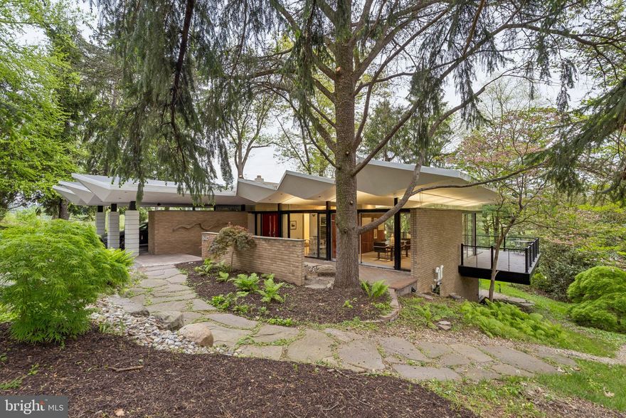 Set at the end of exclusive Monk Road on the cul-de-sac, this Midcentury Modern masterpiece by noted architect Irwin Stein is a rare expression of thoughtful design, natural beauty, and timeless livability in the heart of Gladwyne. Built into a picturesque hillside overlooking wooded surroundings above the Schuylkill River, the residence embraces its setting through expansive glass, abundant exposures, and a seamless connection to landscape from nearly every room.  The dynamic "folded plate" roof, a signature of Steins, appears to float above the home.

A paved patio leads to the ground-level entrance, where a bright and welcoming foyer immediately showcases the home's generous proportions and architectural character. Original details blend effortlessly with tasteful updates, while Stein’s signature approach to light and sightlines is evident throughout—framing mature trees, natural foliage, and long views at every turn.

The main level offers an ideal everyday layout. The primary suite is privately positioned and includes an ensuite bath and copious closets. Two additional bedrooms on this floor enjoy large windows, tranquil views of the property, and share a full hall bathroom. Nearby, the updated kitchen, clad on three sides with original Walnut boards, features granite countertops, stainless steel appliances, and an electric cooktop, while the adjacent dining room is perfectly placed for both casual meals and entertaining. There is also an expansive, sunken living room highlighted by a fireplace, butt-glazed corner glass windows and a surrounding deck. 

Downstairs, a more intimate family room creates a warm and inviting gathering space centered around a cozy fireplace. Designed for entertaining and relaxed living alike, this level also includes two additional well-sized bedrooms sharing a full hall bath, offering flexibility for guests, offices, or fitness needs.  There is also an expansive bonus room ready to be made into a home gym or craft center and the original bomb shelter (the home was designed in the sixties!) ready to be converted into a wine cellar.  

Glass doors open directly onto an organically shaped custom patio with unique rock formations that catch the water as it plunges from the roof on rainy days; it's where the home’s indoor-outdoor lifestyle truly shines. A few steps down into the yard, a heated in-ground pool set against a dramatic stone wall provides the perfect summer retreat.

Completing the property is a covered carport equipped with a Tesla electric charger, thoughtfully integrated for modern convenience. Surrounded by wooded scenery and elevated river views, this exceptional residence offers a rare opportunity to own a true architectural gem in one of the Main Line’s most coveted settings.