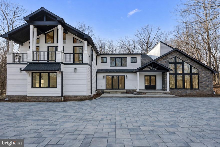 An exceptional new construction 4 bedroom, 4 ½ bath residence set on ten private, wooded acres in Upper Makefield Township.  This striking contemporary estate offers approximately 5,400 square feet of finished living space designed for refined modern living. Approached by a long driveway with a private gated entrance and monitored entry.  The setting immediately establishes privacy, serenity, and a true sense of arrival.
Architecturally designed by Luce Architects with thoughtfully selected interiors by Georgio Savva, the home reflects a sophisticated yet understated aesthetic throughout. Wide-plank white oak floors, Marvin windows, Kohler fixtures, and clean architectural lines create a seamless blend of warmth and modern elegance across four bedrooms and beautifully appointed living spaces.
The open first floor layout is both dramatic and functional, featuring soaring ceilings, exposed beams, designer lighting, and a stunning stone fireplace anchoring the great room. Walls of windows and expansive glass doors flood the interior with natural light and connect effortlessly to the surrounding landscape. The gourmet kitchen is a true showpiece, offering dual quartz islands with abundant storage, paneled Thermador refrigeration with integrated wine storage, double ovens, a built-in espresso station, and a fully equipped walk-in butler’s pantry with second sink and dishwasher. The kitchen and dining areas flow together perfectly for entertaining or everyday living.
The main level also includes a private office, stylish powder room, custom mudroom with built-ins, and interior access to an oversized three-car garage. Upstairs, three spacious secondary bedrooms each feature ample closet space and refined en-suite or adjacent baths with walk-in glass showers and elegant vanities.
The primary suite serves as a tranquil retreat, showcasing custom millwork, dual Built in closets, and a spa-inspired bath with soaking tub, double vanity, vaulted ceilings, and an oversized two-person walk-in shower. Sliding doors lead directly to a front patio, offering peaceful woodland views and a quiet place to unwind.
The three other bedroom all have their own full bathrooms and built-in closets.  A fully finished lower level provides flexible space ideal for a wine cellar, fitness or wellness studio, media room, or additional entertaining area. Privately positioned yet conveniently located just minutes from New Hope, Newtown, and major commuter routes, this remarkable property offers luxury living surrounded by nature in Upper Makefield, one of Bucks County’s most desirable settings.  Note:  some of the pictures have been digitally enhanced.