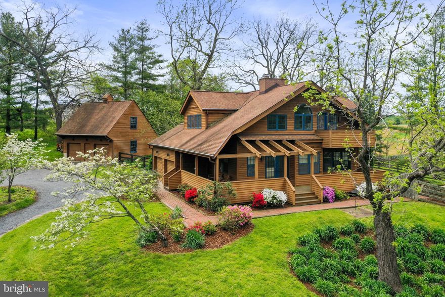 Custom Built Contemporary Bungalow design was Woman's Day Magazine 1982 Award Winning "Small House with Lovely Living Space".  “Communicates a big house feeling by ingeniously incorporating old and new design concepts”.  In the heart of horse and wine country, 10+ acres of arguably the most beautiful land Loudoun County has to offer. This stunning property invites one to wander gently through rolling pathways through majestic trees, over bridges spanning a robust stream, to a scenic pond, and even fruit trees.  There is an inground pool just so you have it all!  Mature landscaping is well thought out with native plantings for low maintenance. Private outdoor living spaces include covered wrap-around porches, brick patio, and pool area all with the most amazing views.
The timeless architectural features include:   
-Arched chimney niche at the top of the stairs brings light to the upstairs hallway and offers a view into the living room
-Primary bedroom has its own balcony and walk-in closet
-Spacious living room has cathedral ceiling and fireplace chimney with brick to the roofline
-Living room offers window storage seat, and formal seating area
-Window from the second level overlooking the living room provides an “interior court” effect from the built-in love seat
-Glass is used extensively to distribute light throughout the house
-Upper bath ceiling rises to the roof line for a luxurious feeling of space
-French doors lead to the porch where trellis roof allows more sun into the living room below
-Large Palladian window on the second floor breaks up the straight lines of the siding
-Cantilevered balcony off primary bedroom
Two bedrooms and renovated bath are in the upper level. Kitchen, laundry, full bath, bedroom/den, dining area, living room, access to the two-car attached garage on the main level. Recreation room, bedroom/den, and workshop/utility room are in the lower level.  In addition to the charming quality-built home, the property also includes a detached two-car garage with large, walk-up, floored attic space. Rare opportunity to own a home and property of this scope; lovingly built and maintained by one owner.