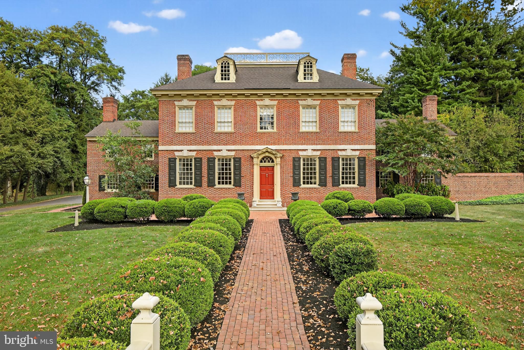 Welcome to an exceptional opportunity to own one of the most distinguished residences in the Wyndham Hills community. Every detail of this exquisite home has been thoughtfully designed and meticulously crafted, blending classic architectural refinement with modern functionality. Set on beautifully landscaped grounds, the home’s stately exterior is enhanced by brick walkways, lush gardens, a gently flowing brook, and a picturesque pedestrian bridge featuring an elegant widow’s walk atop the roof. Additional architectural highlights include handcrafted moldings, and stone lintels over the windows. Upon entering, the grand two-story foyer immediately sets the tone with detailed millwork and architectural sophistication. The formal living room exudes warmth and elegance with its floor-to-ceiling raised paneling, gas fireplace, wainscoting, dentil crown molding, and custom full-length window treatments. Designed for both work and leisure, the home features a spacious office with custom built-in cabinetry and a bay window, as well as a richly paneled den with an inviting fireplace and sweeping views of the gardens through oversized windows, perfect for quiet moments or gracious entertaining. The formal dining room is ideal for gatherings both intimate and grand, boasting intricate moldings, a gas fireplace, a solid brass chandelier, and built-in cabinetry. Throughout the home, hand-blown glass windows flood each room with natural light, while dark-stained Southern Yellow Pine flooring lends warmth and historic charm. The heart of the home is the thoughtfully renovated kitchen, a true chef’s delight outfitted with custom cabinetry, top-of-the-line Sub-Zero, Thermador, and Bosch appliances, Brizo fixtures, and a charming breakfast area with bay window views of the rear patio and gardens. A custom walnut desk and pantry add both function and beauty to this inviting space. From here, a rear staircase leads to a private suite complete with a fireplace, full bath, and sitting area, ideal for guests or a private retreat. Additional main-level features include a mudroom with brick flooring, a charming powder room, and a flexible room that could serve as an additional bedroom or office. The second floor offers three generously sized bedrooms, each with walk-in closets, built-in cabinetry, and hardwood flooring. A spacious hall bath with double vanities and marble countertops serves these rooms. The luxurious primary suite is a true sanctuary, featuring floor-to-ceiling paneling, a gas fireplace, a beautifully appointed bath with oversized walk-in shower and custom cabinetry, and a dressing room with solid cherry built-ins. A dedicated laundry room, exercise room, and walk-in storage closet complete the upper level. Outside, a covered walkway leads to the detached, all-brick, oversized three-car garage. This two-story structure features a private guest suite, currently used as an entertainment space. Complete with kitchenette, full bath, and flexible living/sleeping areas. Set on breathtaking grounds, the property also includes an all-brick gardening building, perfect for hobbyists or outdoor entertaining. This exceptional residence is a rare offering that combines timeless design, luxurious finishes, and a setting of unmatched beauty. Don’t miss the opportunity to experience this remarkable home, schedule your private tour today.