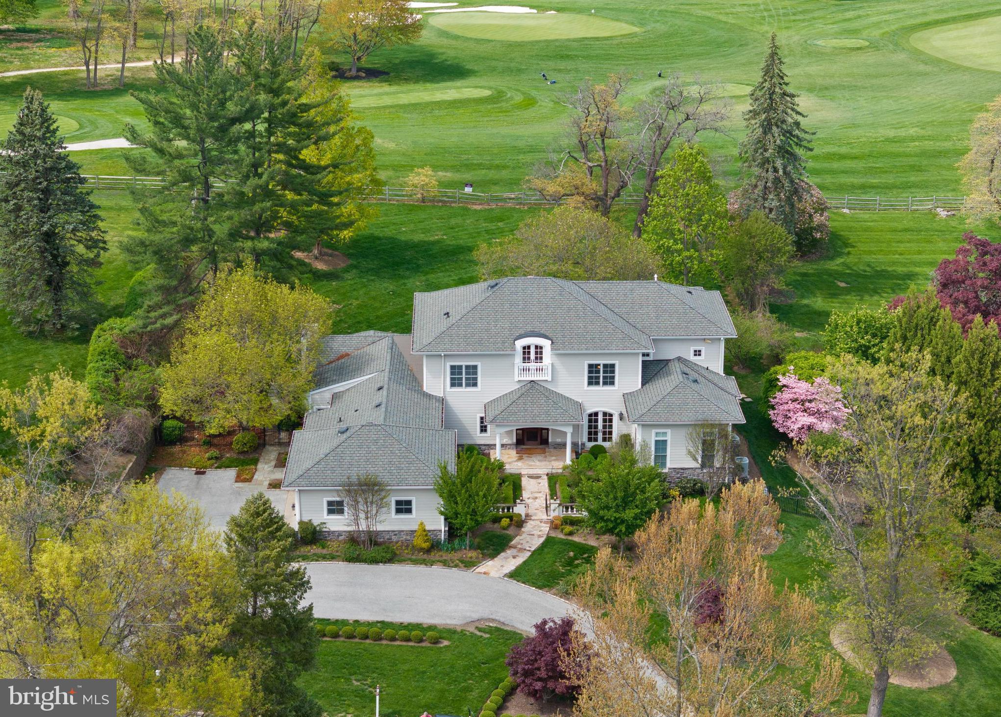 Welcome to this custom-built, over 6,500 sq ft architectural masterpiece, peacefully perched along the 3rd fairway of the Philadelphia Country Club. Perfectly positioned to capture breathtaking, golf course views, this remarkable residence offers the rare opportunity to live in harmony with nature, all while enjoying the sophistication of thoughtfully designed interiors. From the moment you step through the front door, you are immediately struck by the grandeur of the soaring two-story Foyer. A sweeping circular staircase anchors the space, setting an elegant tone that seamlessly transitions throughout the home. The open floor plan is a celebration of light and space, where natural light pours in from every angle through oversized windows that frame the picturesque golf course backdrop. The flow between formal and informal spaces is effortless, ideal for both grand entertaining and intimate daily living. The Formal Living & Dining rooms offer refined millwork and architectural detail, while the expansive sunken Great Room exudes warmth and character with its commanding stone fireplace and French doors that draw in the beauty of the outdoors. Sunken into this space is a custom built-in Bar—an ideal setting to sit and enjoy a drink while taking in the ambiance of the fireplace and the serene outdoor setting beyond. Extending the full length of the home is a fabulous flagstone Patio partially covered that serves as a true outdoor living room, providing the perfect space for year-round enjoyment. This stunning feature can be accessed from the Great Room, Living Room, and Dining Room, creating effortless indoor-outdoor flow and making it an entertainer’s dream. A Gourmet Kitchen sits at the heart of the home, beautifully appointed with high-end appliances, custom cabinetry, a spacious center island, and a walk-in pantry. Just off the Kitchen, the Breakfast Area features a custom built-in banquette, creating an inviting and functional space for casual meals and gatherings. One of the most coveted features is the first-floor Primary Suite—a true sanctuary—featuring a cozy fireplace, separate his and her walk-in closets, and a luxurious spa-like Bathroom complete with steam shower. Also located on the main level is a 2nd Bedroom that is currently transformed into the most precious nursery, adding versatility and warmth to the home’s layout. The Main Level is completed by a richly appointed home office, where custom mahogany built-in bookcases, cabinetry, & fireplace create a warm, sophisticated environment. A Formal Powder Room is conveniently located off the Foyer, while an Informal Powder Room is thoughtfully tucked near the Mudroom. The Mudroom also provides direct access to the oversized Garage, which offers ample space for vehicles and storage, and is equipped with an electric vehicle charging plug, blending practicality with modern luxury. Ascend to the 2nd floor via the sweeping staircase, where an open balcony captures the exquisite Foyer below and connects four additional Bedrooms. 3 of the Bedrooms are ensuite, each with beautifully updated Baths, offering comfort and privacy for family and guests alike. The 4th Bedroom is generously sized and can serve as an additional guest room, playroom, or upstairs office with an outdoor balcony. The finished walk-out Lower Level offers endless possibilities for recreation and relaxation, with abundant natural light and direct access to the backyard. This level includes a Full Bathroom and can easily accommodate a home gym, game room, wine cellar, or home theater, allowing you to tailor the space to your lifestyle. The grounds are equally impressive with a manicured lawn, lush landscaping, and the showstopping covered Porch that ties it all together—an extraordinary setting for entertaining, relaxing, and taking in the serene views of the Fairway. This exceptional home in Gladwyne is a rare opportunity to live luxuriously on a Main Line Golf Course!! Showings begin May 1st.