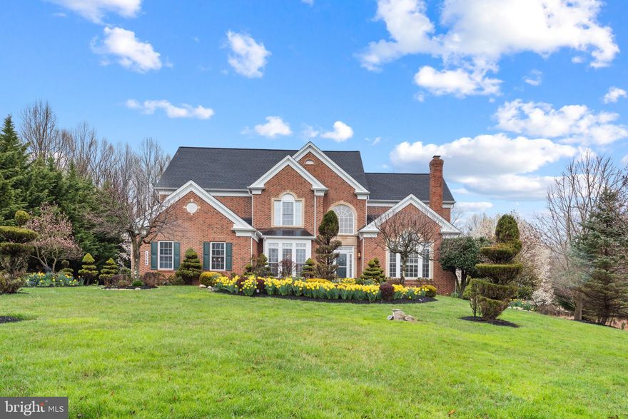 Backing to trees and situated on a .76 acre homesite in Paddocks East is a harmonious blend of modern and classic architectural elements with a total of 6,702 sqft of living space spread over three floors is this stunning brick manor home. An elegant 2-story foyer with a bright Palladian window introduces this home with many design elements which continue throughout this exciting residence beginning with beautiful hardwoods, French doors to a study displaying a coffered ceiling and custom shelving flanking an ambient fireplace and a Palladian topped picture window, and a formal dining room accentuated by a box bay window, large profile crown moldings, chair rail trim, and wainscoting.  Casual living area designed for today’s busy lifestyles is found in the soaring two-story family room directing your attention to a marble surround see-through gas fireplace completed with a decorative trim selection creating a cozy ambiance sure to impress your guests, plant shelving circling half the room, 2 levels of windows, walkouts to a party-sized deck with a pergola spanning the length of the home, casual stairs to the bedroom level and 2nd floor overlook, and amazing natural light and wooded views. The cooktop in the curved island with breakfast bar, double oven, and pass-thru pantry add to the well-appointed kitchen, while the massive rear porch presents a fireplace and summer kitchen, plentiful 42" white wood cabinetry, sleek counters and prep space, a planning desk, and stainless steel appliances add to the well-appointed kitchen in this epicurean’s delight room extended by a breakfast room with a bay architecture, a vaulted ceiling, a shared fireplace, French door access to massive rear deck with a pergola and steps to a tree-lined backyard. Additional living areas are still to be seen in the upper level with five bedrooms including a spacious owner’s suite presenting a deep tray ceiling with stylish etched moldings, an open sitting room area with a bay window, a walk-in closet, and a luxe bath showing a double vanity, a glass enclosed shower, and a jetted soaking tub. Tucked in the lower level are more livable spaces allowing you to customize to your entertainment needs and is highlighted by a rec room with a walkout, recessed lighting, and a games area, a bedroom with a walk-in closet, a full bath, and great storage.
