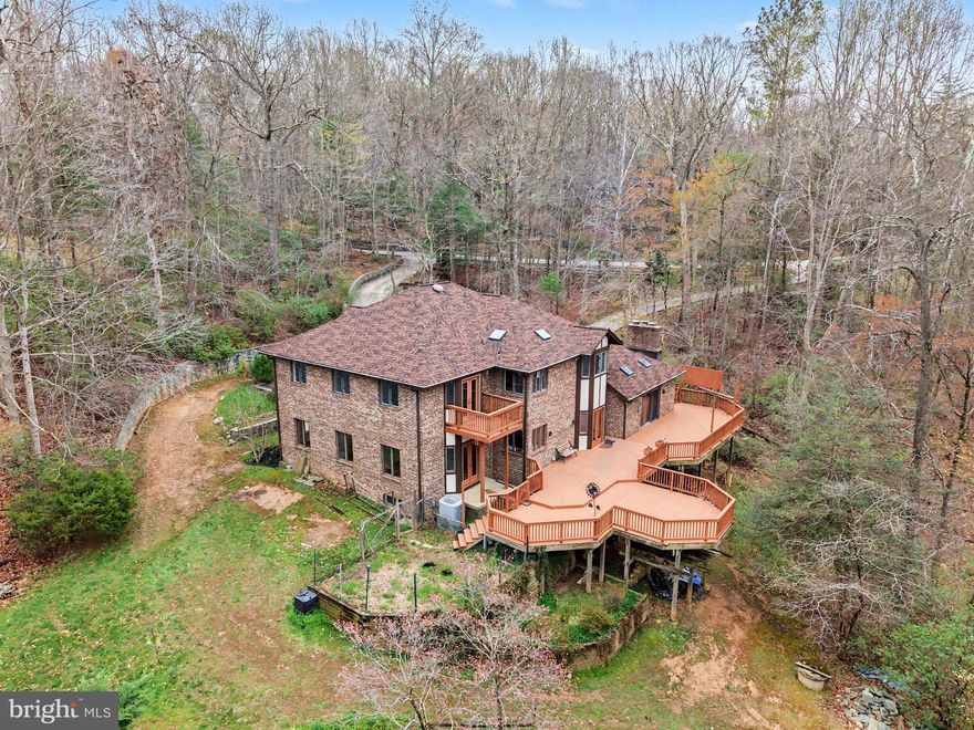 Tucked away in the prestigious Cathedral Forest community of Fairfax Station, this extraordinary custom home is being offered for the very first time by its original owner. Privately situated on 6.6 wooded acres, the property offers breathtaking views, complete privacy, and the rare opportunity to enjoy the beauty of nature without the upkeep —deer and other woodland wildlife are often right outside your window.
From the moment you arrive, the home makes a grand impression with its stately presence, expansive front patio, wraparound driveway, and two-car garage. Step inside to a dramatic two-story foyer filled with natural light and an airy, open feel throughout. The main level is designed for both everyday living and elegant entertaining. Newly refinished hardwood floors flow throughout the space. Just off the foyer is a private office or optional main-level bedroom, conveniently located next to a full bath. The formal dining room opens seamlessly to the spacious living room, creating the perfect setting for hosting gatherings.
At the heart of the home is the beautiful kitchen, featuring custom cabinetry, a large eat-in area, and views of the surrounding trees. The adjacent family room is warm and inviting, centered around a stunning stone fireplace and filled with natural light. From the kitchen, step out onto the rear deck and take in the peaceful wooded views and serene setting. Upstairs, you’ll find four spacious, light-filled bedrooms. The expansive primary suite includes an additional sitting room that could easily serve as a private office, nursery, or retreat. Every bedroom offers generous space and beautiful natural light. The walkout lower level is unfinished, but the possibilities are endless. With high ceilings, a window, exterior door, and space already ideal for an additional recreation room with a fireplace, this level offers tremendous potential to create significant additional living space and value. The mature Cathedral Forest neighborhood is known for its privacy, established setting, and beautiful homes. While there is plenty of usable side yard space for outdoor enjoyment, the majority of the acreage is wooded—allowing you to enjoy the spectacular views and natural surroundings without the maintenance of open land. A truly special property offering privacy, scale, timeless design, and endless possibilities in one of Fairfax Station’s most desirable neighborhoods.