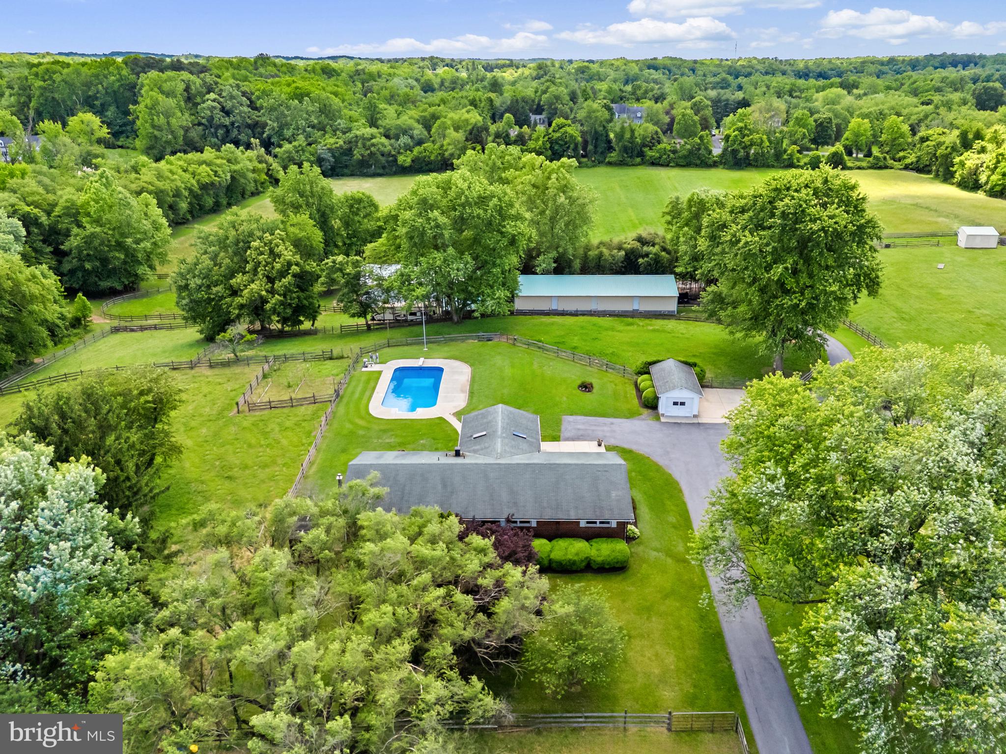 Welcome to Windimurra Farm in Davidsonville, Maryland, a rare opportunity to own over 22 acres of premium land in one of Anne Arundel County’s most desirable and rural settings. Large parcels like this are becoming increasingly scarce in Davidsonville, especially those served by its award-winning schools and located just 15 minutes from Annapolis and 45 minutes from Washington, D.C. This property offers the ideal combination of privacy, functionality, and accessibility.
The main residence is a spacious and comfortable 4-bedroom, 3-bathroom home with over 3,000 square feet of finished living space. A highlight of the home is the screened-in porch overlooking the pool—perfect for relaxing while taking in views of the surrounding farmland. A detached garage provides covered parking and additional storage.
Designed for equestrian use, the property is a fully operational horse farm that has been carefully laid out under guidance from the University of Maryland Extension Service. The resulting layout supports rotational grazing. The paddocks feed into common hard-stand areas which are fitted with run-in sheds, netted hay feeders, and watering points. This configuration facilitates pasture management and use, providing superior grazing conditions.
Ten stalls are housed in the lower level of the bank barn. The lower level includes, a wash stall, feed room, tack room, bathroom, laundry, and an office/sitting area. The upper level of the barn provides storage for up to 3,000 bales of hay. The property produces hay providing an excellent feed source for the farm or potential for income. Additional features of the property include a 100’ by 200’ outdoor riding arena, round pen, small animal shed, composting area, vegetable garden, and a 1-acre spring fed pond.
The property has a large workshop designed to support both farm operations and mechanical work. With over 2,800 square feet and 14+ foot ceilings, the shop includes a full-size auto lift, 220-volt and 120-volt outlets and compressed air outlets throughout. It is equipped with a separate HVAC system, and its own hot water heater, making it an essential and highly functional space for anyone needing serious workspace.
Whether you’re seeking a private country estate, a turn-key horse operation, or a unique long-term investment in land, 965 Mount Airy Road offers a rare blend of lifestyle, location, and land value in the heart of Davidsonville.