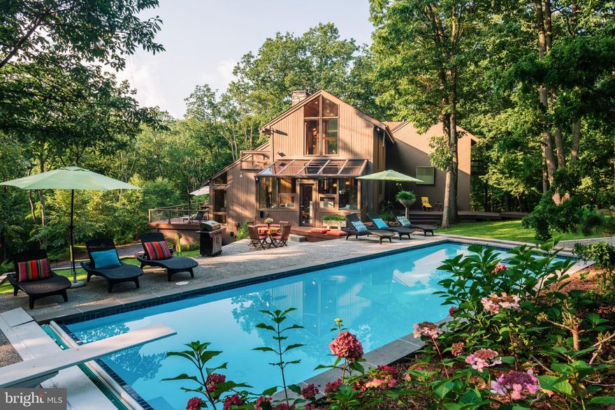 This one-of-a-kind property is more than just a home; it's a rare mid-century modern retreat for those craving beauty, privacy, and a distinctive lifestyle. 

Perched on 6.5 wooded acres in northeastern Lancaster County, this architectural treasure offers the feeling of being tucked away in your own private resort, yet close to everything that matters. It's a place where mornings feel peaceful, evenings feel cinematic, and every season brings its own kind of magic. 

Seamlessly integrated into its forest-like setting, this lovingly maintained property blends architectural character with thoughtful 21st century updates. Inspired by an architect mentored in the tradition of Frank Lloyd Wright, the home preserves its original custom contemporary design while delivering modern comfort and resort-style living. 

A floating walkway leads to a hand-carved teak door and dramatic light-filled interior featuring soaring ceilings, skylights, mirrored walls, and expansive glass. Everywhere you look, the outdoors feels close enough to touch. 

The main level offers an open dining area with black granite floors, a chef's kitchen with Viking and Thermador professional appliances, and quartz waterfall island, and a sunlit solarium/breakfast room. 

The spectacular great room showcases vaulted knot-free cedar ceilings, floor-to-ceiling built-ins with library ladder, a fireplace, bar, and French doors opening to a large deck with sweeping sunset views of Texter Mountain. 

This home features multiple bedrooms and flexible living spaces, including a library/home office and guest accommodations with a Jack-and-Jill bath and two exceptional primary suites.  

The 32 x18 primary suite is a retreat within a retreat--original teak parquet floors, soaring cedar ceilings, a private deck and a custom California Closet walk-in.  The Porcelanosa bath feels like a spa with radiant heated floors, under-vanity lighting, and a curbless waterfall-mosaic shower.  A connected den with built-ins offers space for a nursery, reading room or a second office.   

A second primary suite offers a cathedral wood ceiling, cozy fireplace, skylights, a custom California Closet and a luxurious Porcelanosa bath with soaking tub and radiant heat floors plus serene views of the pool and game lawn from its private deck. 

The lower level provides a large multi-purpose recreation area, home gym with climate control, full bath, laundry room, workshop, and ample storage. 

Outdoors enjoy true resort-style living with a heated swimming pool, a lawn for outdoor games, and serene wooded privacy, perfect for relaxing or entertaining.  

Additional features include two double-car garages with one being heated, equipment storage, and close proximity to recreation, including Blue Marsh Lake, Galen Hall Golf Course, Mount Gretna, cycling routes, walking trails, and the vibrant dining scene of Lancaster. Convenient access to I-76 places Philadelphia, New York City, Washington, D.C., and the Jersey and Maryland shores within easy reach.  

This is the kind of home people remember.  It's where holidays become traditions, summers seem to last forever, winters feel like a scene from a holiday movie and everyday moments feel elevated by the beauty around you.  It's a home that invites you to slow down, breathe deeper and live more fully.

Priced below professional appraisal, this home is waiting for you to become its new owner.