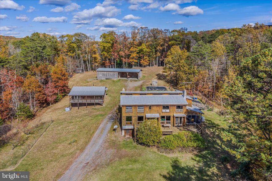 Artist Retreat & Mixed-Use Sanctuary on 32.13 Unrestricted Acres — Berkeley Springs, WV
Welcome to the center of the universe — where the stars align in the rural countryside of Berkeley Springs! This one-of-a-kind property blends naturalist living with industrial artistry on 32.13 acres of unrestricted solitude. Designed for creativity, sustainability, and self-sufficiency, it offers multiple buildings and limitless potential for live/work uses, workshops, studios, or retreats.
The rustic contemporary passive solar home features:
    A dramatic wall of south-facing windows capturing natural light,
    Custom-crafted thick pine floors milled locally,
    Solid oak framing and soaring ceilings with open lofts for additional sleeping or studio space,
    Vermont Castings stove with stone surround,
     Central heat & air installed in 2012,
    Kitchen with an additional antique cookstove,
    Multiple decks and porches — including a screened porch designed to support a hot tub,
    Whole-house generator for peace of mind,
    Full improved unfinished basement — spacious enough to house large-scale projects.
The pole barn/run-in shed offers flexible workshop with water and electric or storage space for every creative endeavor.
The office/studio or guest quarters includes a full covered porch, water, electric, and a wood stove — ready to be completed to your vision, storage below is big enough for tractors.
Nestled among the trees, the chapel provides a serene haven for meditation, yoga, or reflection.
A little further into the property, the hunting shack offers opportunities for wildlife observation or sport, with drop-down windows for watching, photographing, or hunting.
The acreage is thoughtfully developed with walking trails,  fruit trees-4 peach, 1 cherry, 1apple- gardens, rain barrels, and kindling boxes for practical off-grid living. There’s even room for chickens!
Whether you’re seeking a private creative sanctuary, a sustainable homestead, or a multi-purpose live/work retreat, this property offers endless inspiration — your quiet refuge and shelter from the storm.
NOTE NUMBER  OF BEDROOM SPACES COUNTED WITH BUILDINGS IN MIND-MAIN HOUSE HAS 2 CURRENT POSSIBLE BEDROOMS WITH SPACE FOR MORE.  5 buildings in total and a few small sheds.
Stove/flu cleaned in spring 2025,
PROFESSIONAL PHOTOS TO FOLLOW