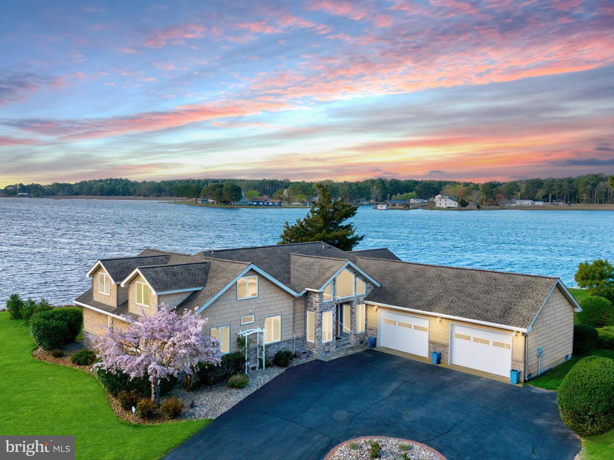 Introducing 13218 Rollie Road E. — a waterfront masterpiece where luxury living meets serene natural beauty. Perfectly positioned on Grays Creek as it opens into the majestic Assawoman Bay, this custom-built residence offers breathtaking panoramic views stretching to the Ocean City skyline. Just minutes from the vibrant beaches and resort towns of Delaware and Maryland, this extraordinary retreat promises the ultimate in coastal living.
Showcasing over 3,000 square feet of meticulously crafted living space, the home offers 5 bedrooms and 4 full baths, each thoughtfully designed to complement the home’s stunning surroundings. Situated on over 200 feet of rip-rapped shoreline, with a 62-foot pier, an 8,000 lb. boat lift, and no HOA restrictions, your waterfront adventures are only limited by your imagination. Step inside and experience a flowing, open-concept layout that was made for entertaining. Walls of picture windows flood the home with natural light and frame ever-changing water views. At the heart of the main living area, a soaring vaulted ceiling crowns the living room, anchored by a floor-to-ceiling stone fireplace with a solid ash mantle—perfectly placed beneath a picture window that captures the skyline of Ocean City. The gourmet kitchen is a chef’s dream, outfitted with 42 inch custom maple cabinetry, dual pantry zones with pull-out shelving, and planning station. Granite countertops provide ample prep and serving space, and the suite of high-end stainless steel appliances includes a 6-burner gas cooktop, range hood, wall oven with warming drawer, drawer microwave, and a U-line wine cooler. Whether it’s casual mornings at the breakfast bar or elegant dinners in the dining room overlooking the bay, every meal here feels like a special occasion. Adjacent to the kitchen, the sun-filled solarium offers a spectacular setting for morning coffee or sunset cocktails, giving you front-row seats to both sunrise and sunset over the water. The primary suite is perfectly positioned to take in peaceful water views. A custom walk-in closet offers exceptional storage and organization, while the spa-inspired ensuite bath features a granite-topped vanity, frameless glass shower, and another picture-perfect bay view from the window. Also on the main level are two beautifully appointed guest bedrooms, each with custom closet systems, two full hall baths, a thoughtfully designed laundry room, interior access to the oversized two-car garage and 16kw generator. From the foyer, a custom oak staircase with handsome railings leads to the upper level, where you’ll find two additional oversized bedrooms, each with spectacular water views, a shared full bath, and multiple storage closets.
Step outside and embrace the tranquility of waterfront living on two expansive decks, where you can relax, entertain, or simply watch the boats glide by. From sunrise to starlight, the unobstructed views and peaceful setting offer a daily reminder of what makes this home so special. 13218 Rollie Road E is more than a home… it’s a lifestyle. A rare offering where timeless craftsmanship, stunning design, and nature’s beauty converge into one unforgettable waterfront retreat.