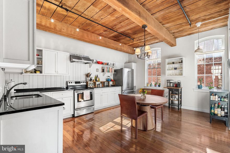 Flooded with natural light from three exposures, this corner home offers an exceptional blend of historic character and modern updates in the heart of Old City. Located on a quiet street, the former warehouse building has been thoughtfully converted into distinctive residential apartments. Originally an open warehouse space, this residence has been professionally designed into a spacious two-bedroom home with private outdoor space, a rare offering in the neighborhood. The entry foyer is lined with oversized factory-style windows and features a large coat closet, an oversized walk-in closet, and a versatile open area ideal for a home office, reading nook, gallery wall, or additional flex space to suit your needs. The open-concept living, dining area and bedrooms feature soaring beamed ceilings, exposed brick, architectural columns, and hardwood floors, creating a dramatic yet comfortable setting for both everyday living and entertaining.
The renovated kitchen is equipped with European-style cabinetry, quartz/Siltstone countertops, a newer suite of stainless steel appliances, and a breakfast bar for additional seating and functionality. A private covered terrace, one of only a limited number in the building, offers outdoor living space ideal for dining or relaxing. The spacious primary bedroom is privately situated and features three oversized windows that fill the room with abundant natural light. Exposed beams and hardwood floors enhance the rooms character, while a walk-in closet provides generous storage.  The second bedroom provides versatility for guests, a home office, or additional living space. The bathroom is appointed with Kohler fixtures, marble, and Italian tile finishes. Additional features include secured basement storage, bike storage and access to a shared roof deck with panoramic city skyline and bridge views. Rental parking is available nearby. Ideally positioned within walking distance to Old City’s restaurants, historic museums, galleries, boutiques, fitness studios, and public transportation, including the Market-Frankford Line, with convenient access to major highways and Philadelphia International Airport. A rare opportunity to own a historic home with private outdoor space, abundant natural light, and authentic architectural details in one of Philadelphia’s most desirable neighborhoods. Welcome Home!