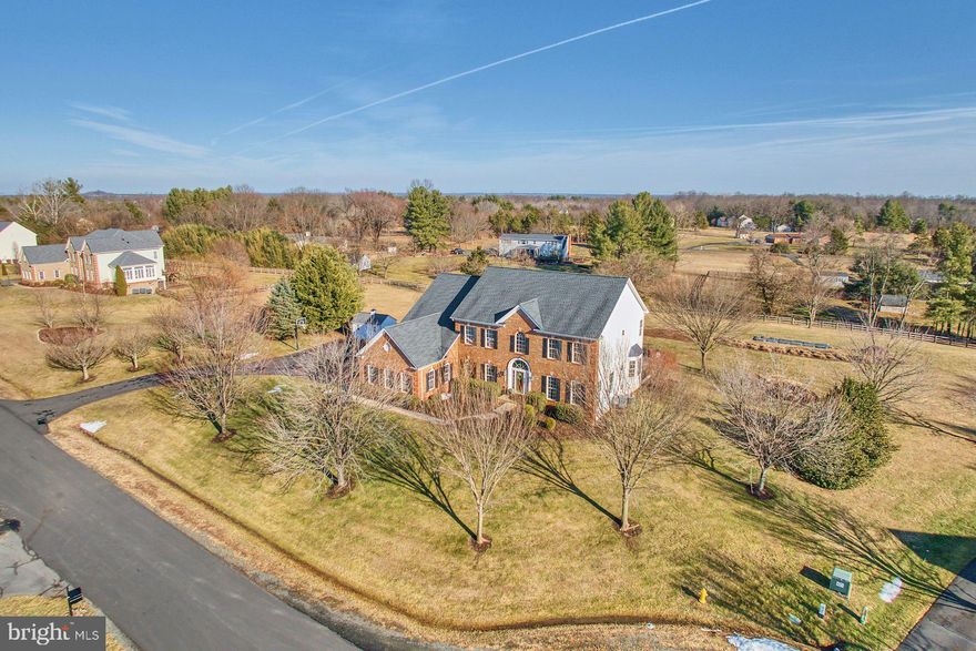 OPEN HOUSE Saturday the 28th from 12-2PM.  Enjoy wine and cheese while you tour this spectacular home.
Commanding presence on 2 private acres in Gainesville’s exclusive Holly Ridge at Lawnvale, this meticulously maintained NVHomes Knightsbridge offers rare turnkey luxury, seclusion, and refined living on a quiet cul-de-sac. Mature trees envelop the property in exceptional privacy and year-round natural beauty.
A dramatic two-story foyer—vaulted ceilings, elegant staircase, striking chandelier, and large arched window high above—welcomes you with breathtaking Shenandoah sunsets framing the entry each evening. Fresh designer paint, crisp white trim, and gleaming hardwood floors create a bright, refined main level. Formal living and dining rooms flow seamlessly into the expansive family room, featuring new carpeting, a stone-surround fireplace, and peaceful wooded views. A private office behind glass French doors, with bay window overlooking blueberry bushes and woods, provides an ideal distraction-free retreat.
The spacious gourmet kitchen boasts white quartz counters and backsplash, generously-sized island, upgraded maple cabinetry, new premium stainless steel appliances, modern cooktop, sunny sitting room, and adjacent sunroom. A butler’s pantry and secondary staircase add everyday convenience.
Outdoor living centers on an expansive Ipe Wood deck built, a patio with afternoon shade, built-in stone fire pit, and sitting wall—ideal for effortless gatherings, grilling, or tranquil mornings with coffee.
Upstairs, four substantial bedrooms include a luxurious primary suite: tray ceiling with chandelier, soft neutrals, dual walk-in closets, and spa-caliber bath with double granite vanities, soaking tub, walk-in shower, and private water closet. The finished lower level offers 9-foot ceilings, designer LVP flooring, vast recreation room with wet bar rough-in, fifth bedroom/full bath (with direct patio access), prepped gym space, and ample storage.
Oversized three-car garage, wide driveway, and whole-home dual-zone audio complete this exceptional offering—rare acreage, thoughtful upgrades, and true move-in perfection in one of Northern Virginia’s most coveted communities. Properties like this vanish quickly—schedule your private tour today.