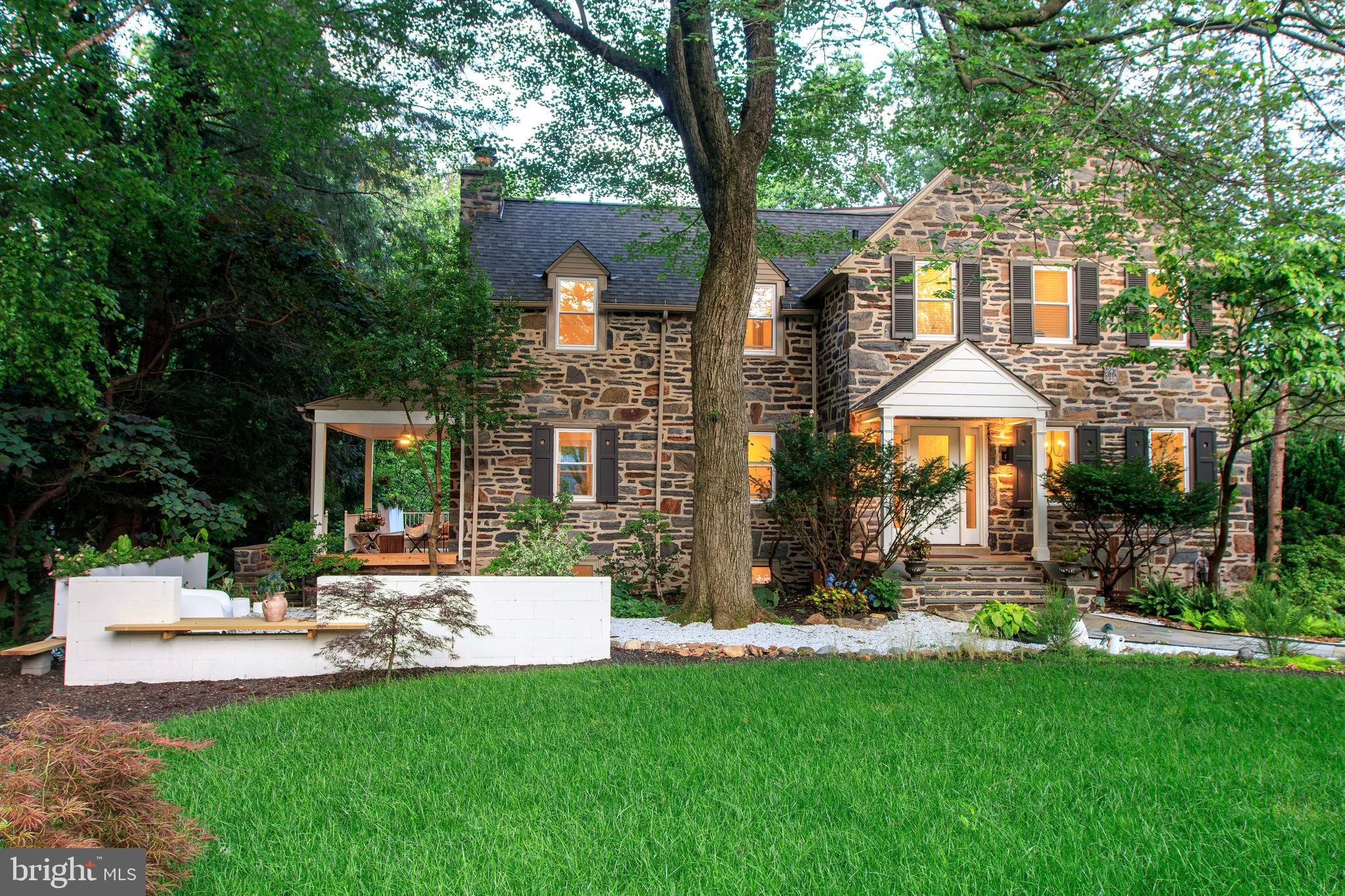 FULL INTERIOR RENOVATION • NEW OPEN-CONCEPT LAYOUT • HIGH-EFFICIENCY WINDOWS & DOORS • TWO FIREPLACES • BUILT-IN BENCHES • FINISHED LOWER LEVEL • MULTI-LEVEL TERRACED GARDENS • FULLY RESODDED LAWN • FLEXIBLE OPEN WORKSHOP / GARAGE • SERENE FOREST RETREAT SETTING
Nestled within the serene woodlands of Lower Merion, this reimagined 1930s stone residence seamlessly blends historic charm with contemporary sophistication. Spanning 3,838 square feet on a lush 0.45-acre lot, the home offers five bedrooms, two and a half baths, and a harmonious flow of indoor and outdoor living spaces. The polished entry welcomes you with gorgeous hardwood floors that extend throughout the home. The bright and airy formal living room features a wood-burning fireplace and access to the expansive wraparound patio, perfect for entertaining or quiet reflection. The open-concept chef’s kitchen and formal dining area are equipped with stainless steel appliances, white cabinetry, a breakfast bar, custom built-in benches, and a cozy fireplace. From here, head to the backyard, enhancing the connection to nature. A dedicated office space and a conveniently located half bath complete the main level. Upstairs, the spacious primary suite offers ample closet space and a luxurious bath with a unique shower and built-in soaking tub. Three generously sized bedrooms and an updated hall bath with a tub provide comfort and privacy. The third floor features a versatile fifth bedroom and additional storage space. The finished lower level offers a family room and a separate laundry area, adding to the home's functionality. Outside, the property is surrounded by mature trees and terraced gardens, providing a rare combination of privacy and openness. Layered patios and a forest living room beyond offer an outdoor extension of life beneath the trees. The garage has been transformed into a flexible open workshop—perfect for creative use, gardening, or storage—while remaining easily convertible for vehicle use. Discover the charm of this ideally located residence in the award-winning Lower Merion School District. Situated just a short stroll from the heart of downtown Narberth, this home offers unparalleled access to local parks, boutique shops, diverse dining options, a historic movie theater, and vibrant community events. Whether you're enjoying a peaceful walk to places of worship or participating in neighborhood festivities, everything you need is within easy reach. This residence is a testament to thoughtful design, where tradition meets modern clarity in a tranquil woodland setting. It is, in essence, a forest retreat—where life flows gently between stone, sun, and trees.