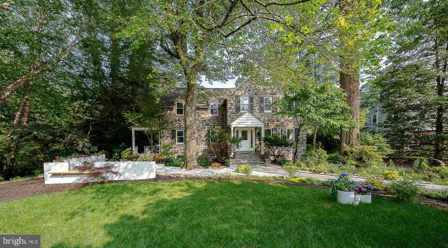Nestled within the serene woodlands of Lower Merion, this reimagined 1930s stone residence seamlessly blends historic charm with contemporary sophistication. Spanning 3,638 square feet on a lush 0.45-acre lot, the home offers five bedrooms, two and a half baths, and a harmonious flow of indoor and outdoor living spaces. The polished entry welcomes you with gorgeous hardwood floors that extend throughout the home. The bright and airy formal living room features a wood-burning fireplace and access to the expansive wraparound patio, perfect for entertaining or quiet reflection. The open-concept chef’s kitchen and formal dining area are equipped with stainless steel appliances, white cabinetry, a breakfast bar, custom built-in benches, and a cozy fireplace. From here, head to the backyard, enhancing the connection to nature. A dedicated office space and a conveniently located half bath complete the main level. Upstairs, the spacious primary suite offers ample closet space and a luxurious bath with a unique shower and soaking tub. Three generously sized bedrooms and an updated hall bath with a tub provide comfort and privacy. The third floor features a versatile fifth bedroom and additional storage space. The finished lower level offers a family room and a separate laundry area, adding to the home's functionality. Outside, the property is surrounded by mature trees and terraced gardens, providing a rare combination of privacy and openness. Layered patios and a forest living room beyond offer an outdoor extension of life beneath the trees. The garage has been transformed into an open workshop, blending indoor creativity with outdoor living. Discover the charm of this ideally located residence in the award-winning Lower Merion School District. Situated just a short stroll from the heart of downtown Narberth, this home offers unparalleled access to local parks, boutique shops, diverse dining options, a historic movie theater, and vibrant community events. Whether you're enjoying a peaceful walk to places of worship or participating in neighborhood festivities, everything you need is within easy reach.  This residence is a testament to thoughtful design, where tradition meets modern clarity in a tranquil woodland setting.