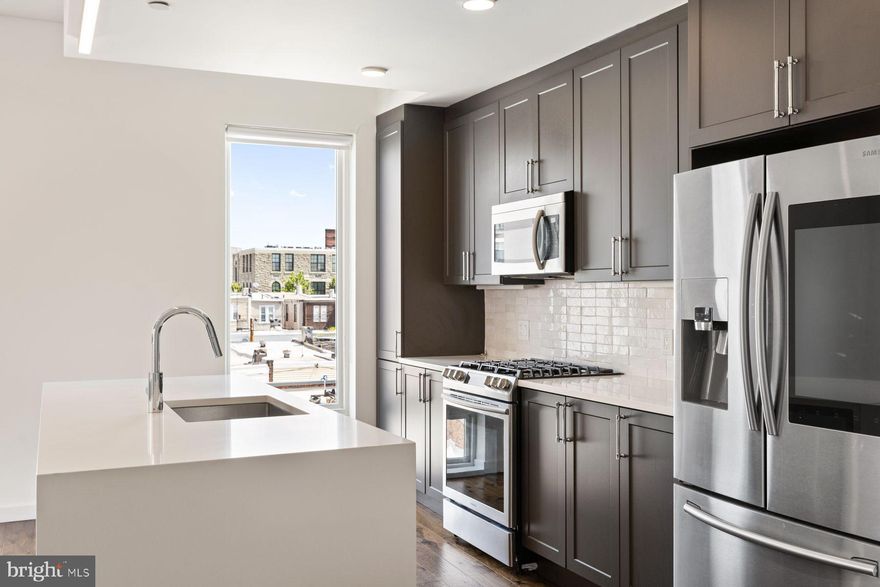 Welcome to Penthouse PH4 at Otto On The Park, a top-floor 2-bedroom, 2-bathroom corner unit offering 1,256 square feet of refined living space and a sprawling 1,300-square-foot private roof deck with panoramic Center City views. Sunlight pours through 7-foot-tall windows, illuminating the open-concept layout that seamlessly connects the smart kitchen—featuring a waterfall island and Samsung Family Hub refrigerator—to the main balcony, perfect for entertaining. The primary suite boasts a walk-in closet and a luxurious en-suite bathroom with dual vanities, a glass-enclosed shower with dual sprayers, and a stone bench. The second bedroom also includes a walk-in closet and is served by a tiled hall bath with a soaking tub. Additional amenities include a laundry closet, coat closets, and an open office nook. Residents enjoy keyless building access, a Nest thermostat, and one deeded, gated parking space. Situated in Brewerytown, PH4 is within walking distance of local favorites like Rival Bros Coffee, Baby's Kusina + Market, New June Bakery,  and Harper's Ice Cream, offering a neighborhood experience unlike most!