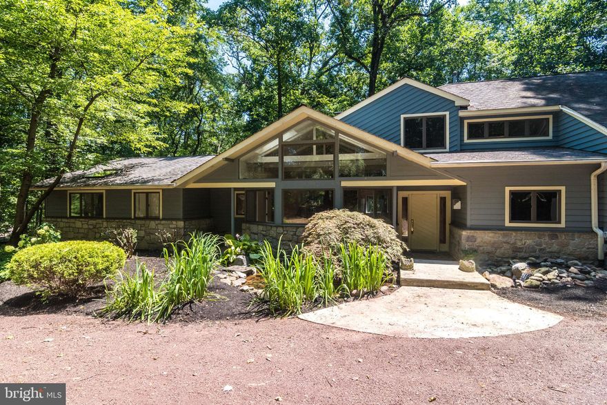 Drawing on elements of California Contemporary design and the last hurrah of the Mid-Century Modern school of architecture, this 4,000 square-foot home is a rare find in Bucks County. Soaring rooflines, floor-to-ceiling windows, and a dramatic floating staircase are just a few its many outstanding features. From the circular driveway, a stone bridge crosses over a koi pond to the front door, which opens to a light-filled living area with hardwood floors and a towering fireplace. The first-level master suite, with its large bathroom and walk-in closet, is tucked away at the eastern end of the house, while the kitchen, dining area, den and laundry room are at the other end. Southern-facing glass doors along the back lead to the dramatic wrap-around deck outside, which, because the house sits on a gently-sloping hillside, feels like it's floating in the treetops. Upstairs are three more bedrooms, one with its own private bath, all featuring raised ceilings and large picture windows. An oversized garage has room for three cars, and a partially finished basement provides even more space for a playroom, work area or additional storage. Set back on a quiet, tree-lined drive with no through-traffic, the wooded property feels completely secluded and private, yet the restaurants, shops and theaters of New Hope and Doylestown are just minutes away, and it's less than an hour's commute to both Princeton and Philadelphia.