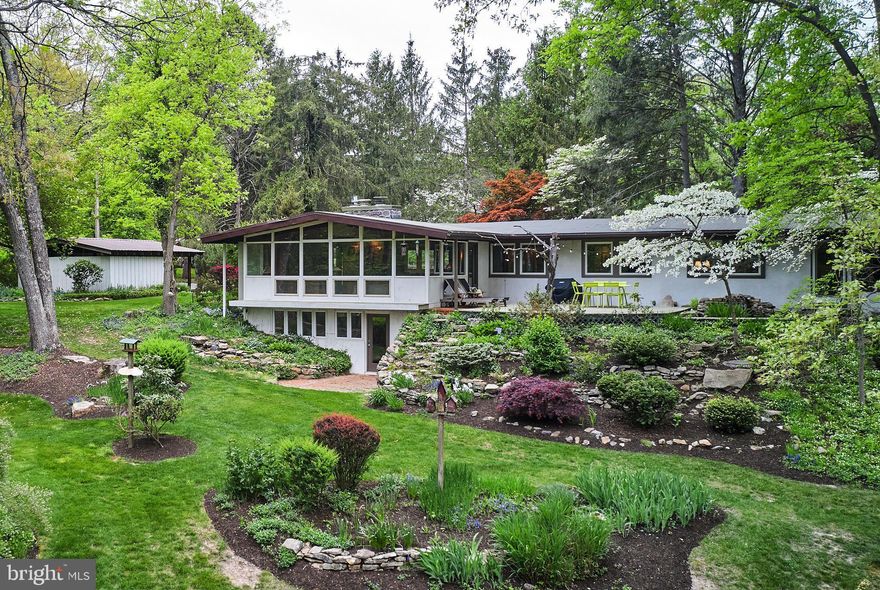 Welcome to a rare gem nestled in Solebury Township – a mid-century modern architectural masterpiece on over seven acres of pristine land. Influenced by the iconic style of Frank Lloyd Wright, this home is a harmonious blend of nature and design, reminiscent of properties more commonly found in California.
With its expansive windows, this single-level living residence seamlessly integrates indoor and outdoor spaces, offering a tranquil retreat from the hustle and bustle of everyday life.
The heart of the home includes a redesigned Bulthaup Studio Kitchen, with Miele appliances and an induction cooktop.  An adjacent kitchen annex with a sink and additional refrigerator adds to the functionality of the space.
The living room is adorned with a gas fireplace, creating a cozy atmosphere for relaxation. A renovated hall bath showcases Bulthaup design and Dornbracht fixtures, while two ample-sized bedrooms offer versatile options for home office space.
The primary bedroom suite is a haven of tranquility.  Large windows bring the beauty of nature indoors, and the custom walk-in closet provides ample storage. The primary bathroom finishes this space with a spa-like setting. With an exit to the backyard deck, you’re invited to a serene Koi pond with a waterfall.
The bright and versatile lower level complete with a beautiful stone fireplace and walk-out backyard  access, currently serves as a spacious family room adjacent to a guest bedroom with full bath.  Outstanding closet space and large storage areas offer practical solutions.
Primrose Creek meanders through the eastern edge of the property, which borders preserved land. Beautiful perennial gardens bloom and provide cut flowers all season long.
Just minutes from the charming towns of New Hope and Lambertville, this home is a true treasure.