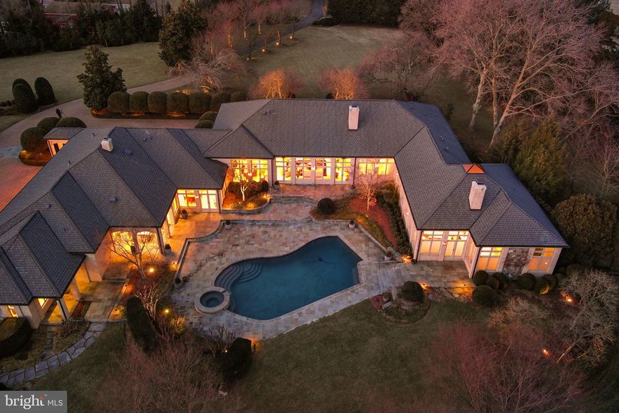 Luxury Oasis in Great Falls – A Private 5-Acre Estate

Tucked away on a private road off Georgetown Pike, this stunning 5-acre estate offers an unparalleled blend of elegance, comfort, and resort-style living. Boasting nearly 9,000 square feet on the Main Level, and 13000 square feet under roof for the ultimate in single-level living. This custom-built home is a masterpiece of design, featuring the highest quality materials, exquisite craftsmanship, and over $1 million in breathtaking landscaping.

Sophisticated Interior & Grand Living Spaces
As you step through the grand mahogany double doors, a magnificent reception hall with hardwood floors and custom moldings welcomes you. The sunken formal living room, with a striking masonry fireplace and expansive views of the pool, creates a warm and inviting atmosphere. Adjacent, the formal dining room also overlooks the outdoor oasis, setting the stage for elegant gatherings.
The chef’s kitchen is a culinary dream, featuring two center islands—one for cooking and another for prep—top-of-the-line appliances, industrial-strength gas cooking, a Sub-Zero refrigerator, black galaxy countertops, and custom flat paneled cherry cabinetry. A spacious Costco pantry, powder room, and garage entry foyer provide additional convenience. The open-concept breakfast area, with walls of glass, seamlessly flows into the family room, which showcases a stunning stone fireplace, custom built-ins, and recessed lighting throughout. Just outside, an outdoor kitchen and private poolside bathroom, featuring a private spa with a sauna, shower. All this elevates the outdoor entertaining experience.

Private Office Wing & Luxurious Bedrooms
A dedicated office wing offers two private offices—ideal for working from home—along with an additional formal powder room. The bedroom wing features five oversized bedrooms, each with en-suite bathrooms, walk-in closets, and recessed lighting.
The primary suite is a sanctuary of relaxation, with a private sitting area, dual-sided fireplace, and direct access to the patio and pool. The spa-like primary bath boasts dual vanities, a soaking tub, an expansive custom closet, and a luxurious shower with multiple showerheads and body sprayers.

Incredible Lower Level & Guest House
The lower level is designed for ultimate entertainment, featuring a stylish sitting area, billiards room, game room, and a custom bar with pendant lighting and natural cherry cabinets as well as black galaxy countertops. Dual pocket doors lead to a state-of-the-art media room with seating for ten. Additional highlights include a spacious exercise room and a powder room.
A separate guest house offers a private retreat with a bedroom, living room, small full kitchen, and bathroom. The quest has its own entrance—ideal for extended stays or an au pair or in law suite.

Resort-Style Outdoor Living
This estate’s outdoor spaces are truly spectacular. A heated inground pool serves as the focal point, visible from most rooms in the home. Lush landscaping, with up-lighting on mature trees, creates a serene ambiance. A sports court, hidden within the landscape, offers the perfect space for basketball enthusiasts. A screened porch overlooks the expansive backyard, providing an additional space to unwind.
The five-car garage is a car collector’s dream, complete with heat and a unique drainage system. The paver driveway, with a front parking area and motor court, enhances the estate’s grand entrance.

An Unparalleled Offering
This extraordinary Great Falls estate offers privacy, luxury, and every imaginable amenity. A true oasis, just minutes from the heart of Great Falls and major commuter routes, yet worlds away in tranquility.
Schedule your private tour today and experience the unmatched beauty of this remarkable home.