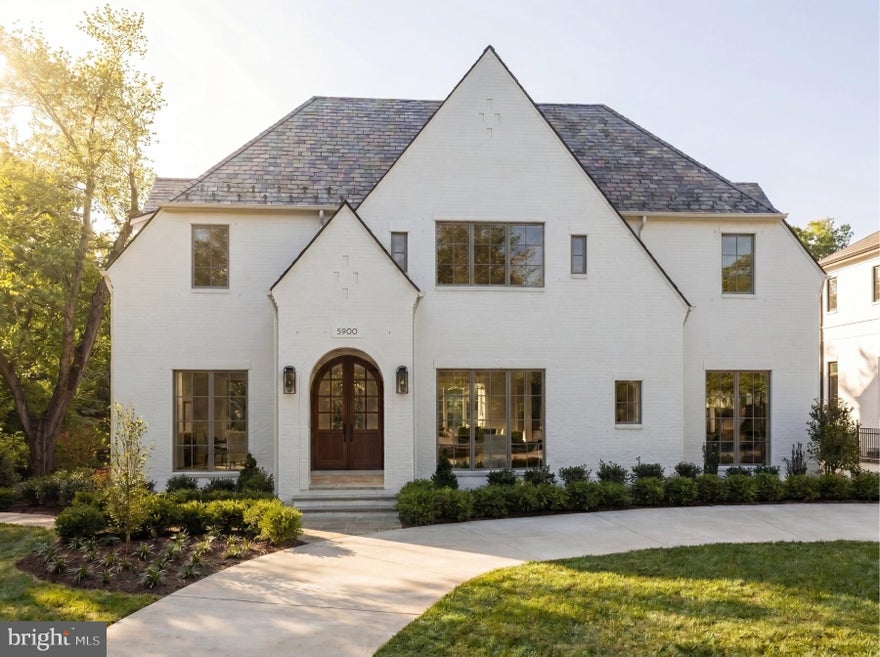 Prominently sited on a prestigious corner lot in the heart of coveted Kenwood, 5900 Kennedy Drive stands as the newest architectural triumph by Terra Innovations, created in collaboration with the acclaimed GTM Architects and the master craftsmen at Castlewood Builders. Conceived as a transitional Tudor, the residence is clad in crisp white brick, an enduring design that merges time-honored English traditions with a contemporary sophistication perfectly suited for modern living.

The home has been deliberately oriented to capture southern exposure, allowing natural light to flood the principal rooms. A unique detached one-car garage complements the concealed two-car side-load garage, maximizing lot usability while preserving green space. A sweeping driveway introduces the stately façade, defined by steeply pitched gables, a slate-style roof, and an arched mahogany-and-glass entry door. Inside, a subtly vaulted foyer sets the stage for 8,808 finished square feet across four thoughtfully designed levels.

A classic center-hall plan anchors the main floor. To one side lies the formal living room, light-filled and inviting. To the other, the dining room is distinguished by a tray ceiling with cove lighting, setting a refined tone for entertaining. A private study with custom built-ins offers a serene retreat and, with access to a full bath, doubles as a main-level bedroom—an ideal option for multigenerational needs.

The open-concept family room forms the heart of the residence, crowned by dramatic ceiling beams and a gas fireplace framed by built-ins. Expansive glass doors open to the covered porch with its own fireplace, pre-wired for screens, heaters, and media, blurring the line between indoor and outdoor living.

At the center of the home is the chef’s kitchen, anchored by a 9-foot artisan island and outfitted with bespoke cabinetry, stone finishes, and top-tier hardware. The 55” Lacanche Classique range serves as both a culinary tool and centerpiece, complemented by GE Monogram appliances. A concealed coffee bar, butler’s pantry, and sunlit breakfast area complete the space. Everyday functionality is enhanced by a mudroom wing with powder room, pantry, laundry hookup, and garage access.

Upstairs, the primary suite offers a sitting area, private terrace, and dual walk-in closets with custom built-ins. The spa-inspired bath features heated floors, a freestanding soaking tub, dual vanities, and a Kohler digital shower. Four additional en-suite bedrooms and a laundry room complete this floor. The top level adds another bedroom, full bath, and family room, all accessible by the home’s four-level elevator.

The lower level is indulgent yet functional. A 32-foot recreation room with wet bar and glass-enclosed wine display serves as its centerpiece. Wellness amenities include a fitness studio, steam shower, and sauna, while a pre-wired golf simulator bay with raised ceilings offers versatility as a recreation or media room. A private au pair suite with exterior access provides independence and flexibility.

Outdoors, the level rear lawn is private and pool-ready, with infrastructure already in place. The home’s location is unmatched, set among Kenwood’s famed cherry blossoms, across from the revitalized Westbard Square, minutes to Downtown Bethesda, and near top-rated schools and commuter routes.

A singular achievement in design, craftsmanship, and livability, 5900 Kennedy Drive establishes a new pinnacle of luxury in one of the Capital Region’s most distinguished neighborhoods.