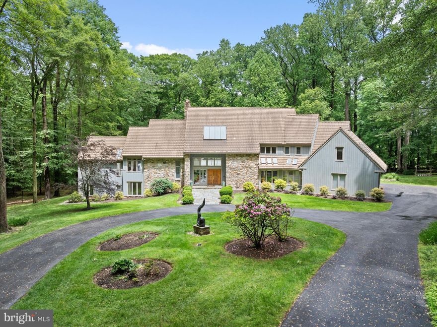 Discover an extraordinary custom‑built contemporary estate, gracefully sited on 6.3 sweeping acres adjacent to the renowned White Manor Country Club Golf Course. Nestled in the heart of coveted Radnor Hunt Country within prestigious Willistown Township, this architectural masterpiece sits at the end of a tranquil cul‑de‑sac on a quiet country lane—offering the ultimate in privacy, elegance, and serene natural beauty. A long, dramatic driveway leads to the grand entrance of this striking stone and cedar residence crowned with an architectural tile concrete roof. Inside, a stunning center‑hall foyer and open floor plan welcome you with a sculptural water feature and fountain, setting the tone for the home’s elevated design. The breathtaking living room showcases floor‑to‑ceiling windows, a refined fireplace, and seamless access to an expansive deck with panoramic views of the resort‑style pool, lush woodlands, and pristine golf course. Designed for effortless entertaining and everyday luxury, the main level flows into a sunlit breakfast area and a sophisticated family room with vaulted ceilings, skylights, custom built‑ins, and an elegant fireplace. The space opens to a sleek, modern gourmet kitchen featuring abundant island seating, premium stainless‑steel appliances, double ovens, and a Gaggenau cooktop—an exceptional workspace for the discerning chef. A formal dining room with tray ceiling and recessed lighting completes this wing. A private main‑level corridor leads to the sumptuous primary suite, an intimate sanctuary with a cozy sitting room and fireplace, private deck access, spacious bedroom, generous walk‑in closets, and a spa‑inspired bath. The home’s thoughtful layout includes a separate back hall with a powder room, laundry room, access to the three‑car garage, and a beautifully appointed second‑story in‑law or guest suite complete with bedroom, living area, and full bath. On the upper level, an airy overlook enhances the sense of openness and leads to an ensuite bedroom plus two additional bedrooms connected by an elegant Jack‑and‑Jill bath. The lower level offers unparalleled entertainment and relaxation. A stylish family room with fireplace opens to a flagstone patio and the pool terrace, flowing into a billiards room, dedicated exercise room, full bath, and sauna—perfect after a summer swim. A wet bar and a private office complete this impressive level. Indulge in outdoor living at its finest with a sparkling pool and jacuzzi, recently replastered with Diamond Brite and enhanced with new drains. Professionally landscaped grounds feature mature specimen plantings, stone walls, stone patios, and multiple viewing decks woven harmoniously throughout the property. Enhancing the estate is a charming art studio or guest retreat with vaulted ceilings, exposed wood beams, skylights, a half bath, and a versatile second‑floor flex space ideal for an office or additional sleeping quarters. This magnificent property offers an unparalleled blend of refined luxury, natural tranquility, and sophisticated design—all within close proximity to major routes, upscale shopping, acclaimed restaurants, and the very best of the Main Line. Immerse yourself in the beauty and grace of this exceptional residence, where elevated living and serene landscapes unite in perfect harmony.
