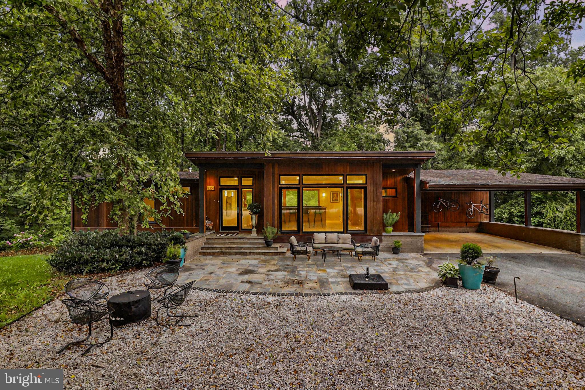 Welcome to 6921 Ayr Ln, a hidden gem tucked away at the top of a peaceful cul-de-sac in the heart of Bannockburn. This exclusive enclave of just 10 homes offers unmatched privacy and tranquility. Nestled beside a wooded lot, the property enjoys a lush, green backdrop—your own private sanctuary in an exceptional natural setting.
This contemporary retreat is a seamless blend of timeless design and modern luxury. With three spacious bedrooms, two and a half beautifully appointed bathrooms, and set on 0.42 acres, the home delivers effortless comfort and sophisticated style. Clean architectural lines, open-concept living spaces, and walls of glass flood the interior with natural light, creating a strong indoor-outdoor connection.
From the street, the home maintains a quiet, refined presence—defined by original wood siding, crisp geometry, and a canopy of mature trees that echo its Mid-Century Modern roots. Step inside, and the atmosphere transforms. Sunlight pours through expansive windows, and the interior opens into a bright, serene escape that invites relaxation and inspires connection.
Whether you’re enjoying peaceful solitude or entertaining with ease, 6921 Ayr Ln is a rare opportunity for modern living in an unparalleled setting.
The main entry level opens into a welcoming flex space directly off the carport. At the center of the home is the open-concept kitchen—featuring custom cabinetry and premium Wolf and Sub-Zero appliances—that flows seamlessly into the adjacent dining and living areas. Laundry and pantry areas are located directly behind the kitchen, making them both convenient and user-friendly. The sun-drenched living room—with its gas fireplace and built-in bookshelves—adds warmth and personality. Designed for everyday living and casual gatherings alike, this space brings people together with ease and comfort.
Two generously sized bedrooms, a stylish powder room, and a full bathroom with dual vanity complete this level—perfect for guests, family, or flexible use.
The garden level, bathed in natural light and with direct access to the backyard, expands the home’s livable space in a thoughtful, functional way. At its heart is a spacious family room with oversized picture windows and a wood-burning fireplace with gas hookup—perfect for cozy evenings, lazy weekend mornings, or casual entertaining. This level also features a private en suite bedroom, complete with wood-paneled ceilings, a built-in desk, a dressing nook, and a sleek bath with an oversized walk-in shower. A wet bar, custom built-ins, and two large storage rooms round out this versatile floor.
Outside, the magic continues. Step into a vibrant community with two neighborhood pool clubs, one just minutes away via a charming wooded path at the end of the cul-de-sac. Located in the highly sought-after Walt Whitman school district and close to walking and hiking trails, this home is just a short drive to Downtown Bethesda, Potomac Village, Whole Foods, and Washington, D.C.
With beloved neighborhood traditions like Food Truck Fridays and an annual talent show, Bannockburn is more than a location—it’s a true community. And 6921 Ayr Ln is your chance to be part of it.