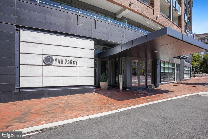 Situated in the heart of downtown Bethesda, this exquisite 2 bedroom den, two bath condo, with 2 garage spots and a storage unit is located in the Darcy, a pet-friendly boutique building with countless amenities. Located on the west-facing side of Woodmont Avenue, this unit highlights stunning sunsets and views into downtown Bethesda. The open floor plan has no shortage of natural light and boasts an inviting foyer that opens into a gorgeous living room with floor-to-ceiling windows, a balcony and a formal dining area.
The gourmet eat-in kitchen features high-end stainless steel appliances, granite countertops,  pantry cabinet and access to an additional balcony with weather proof flooring .
This unit also conveys two garage parking spots and an additional storage unit. The Darcy is situated in a wonderful urban environment, just steps away from the Metro and downtown Bethesda, with shops, restaurants, grocery stores, and biking/walking trails, plus close proximity to downtown DC and Friendship Heights.
Building amenities include an elegant lobby that was renovated and designed by Barry Dixon with 24-hour concierge, a club room with a fireplace, balcony, and catering kitchen, a business center, a private fitness center with a separate yoga studio, and two guest hospitality suites for residents.